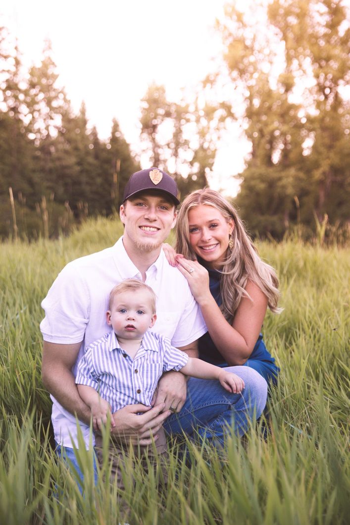 A man and woman are sitting in a field holding a baby.