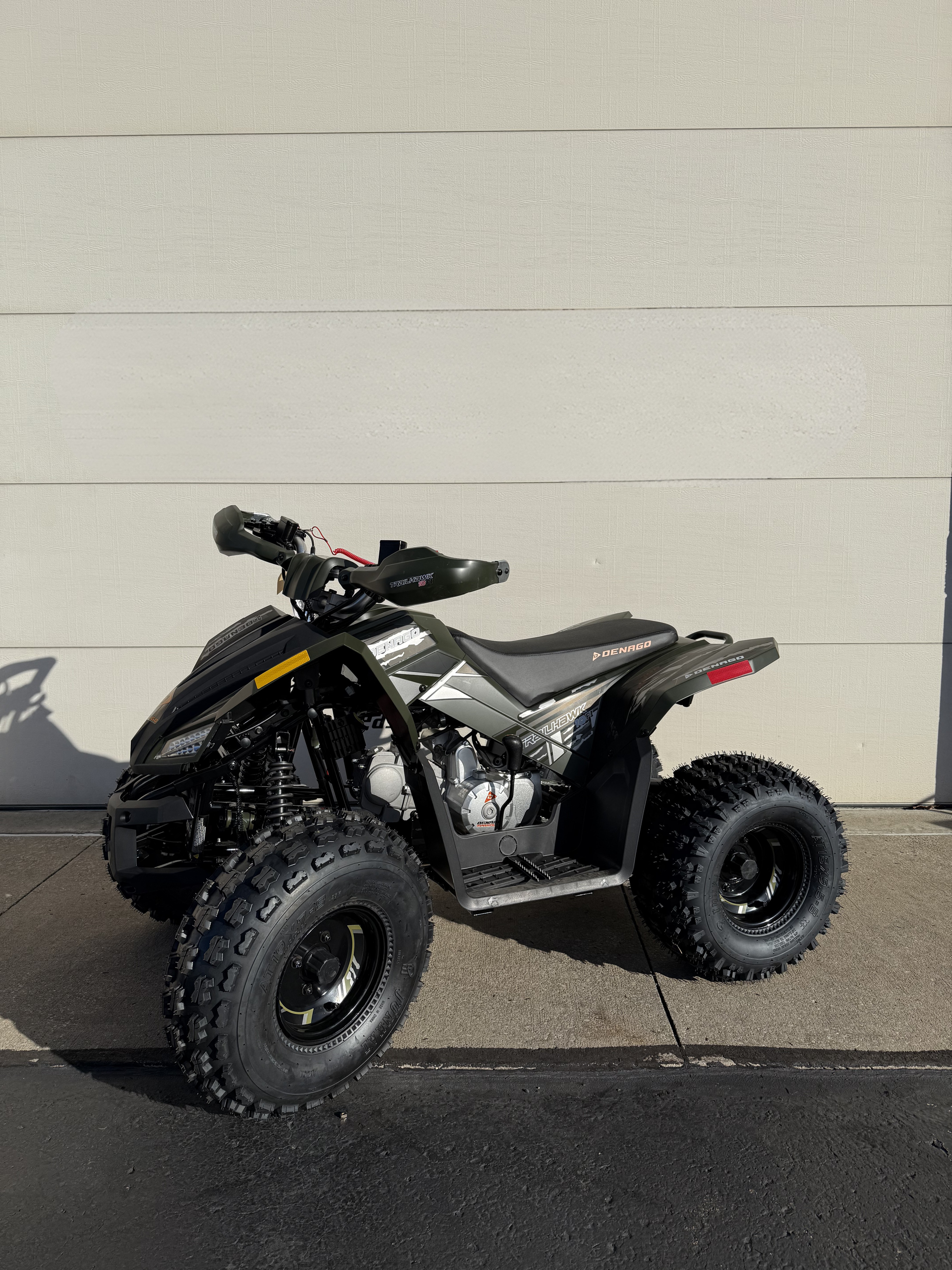 A gray and black all-terrain vehicle (ATV) parked on a paved surface in front of a light-colored wall.