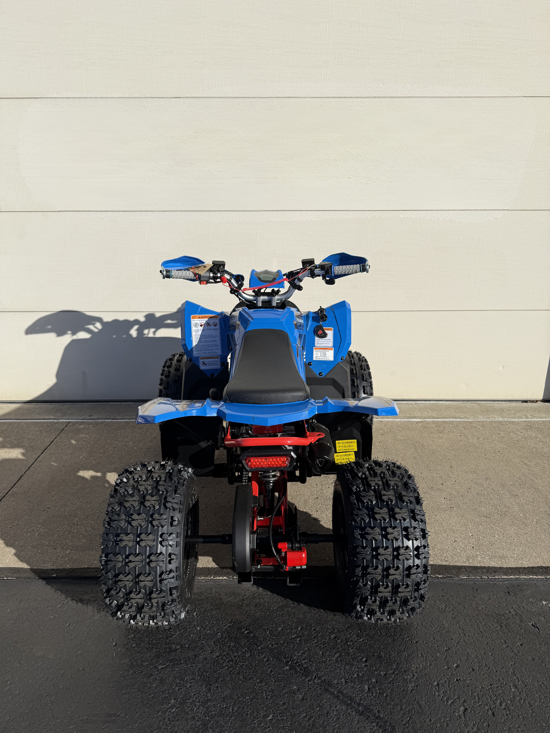 Rear view of a blue all-terrain vehicle parked on a paved surface against a white wall.