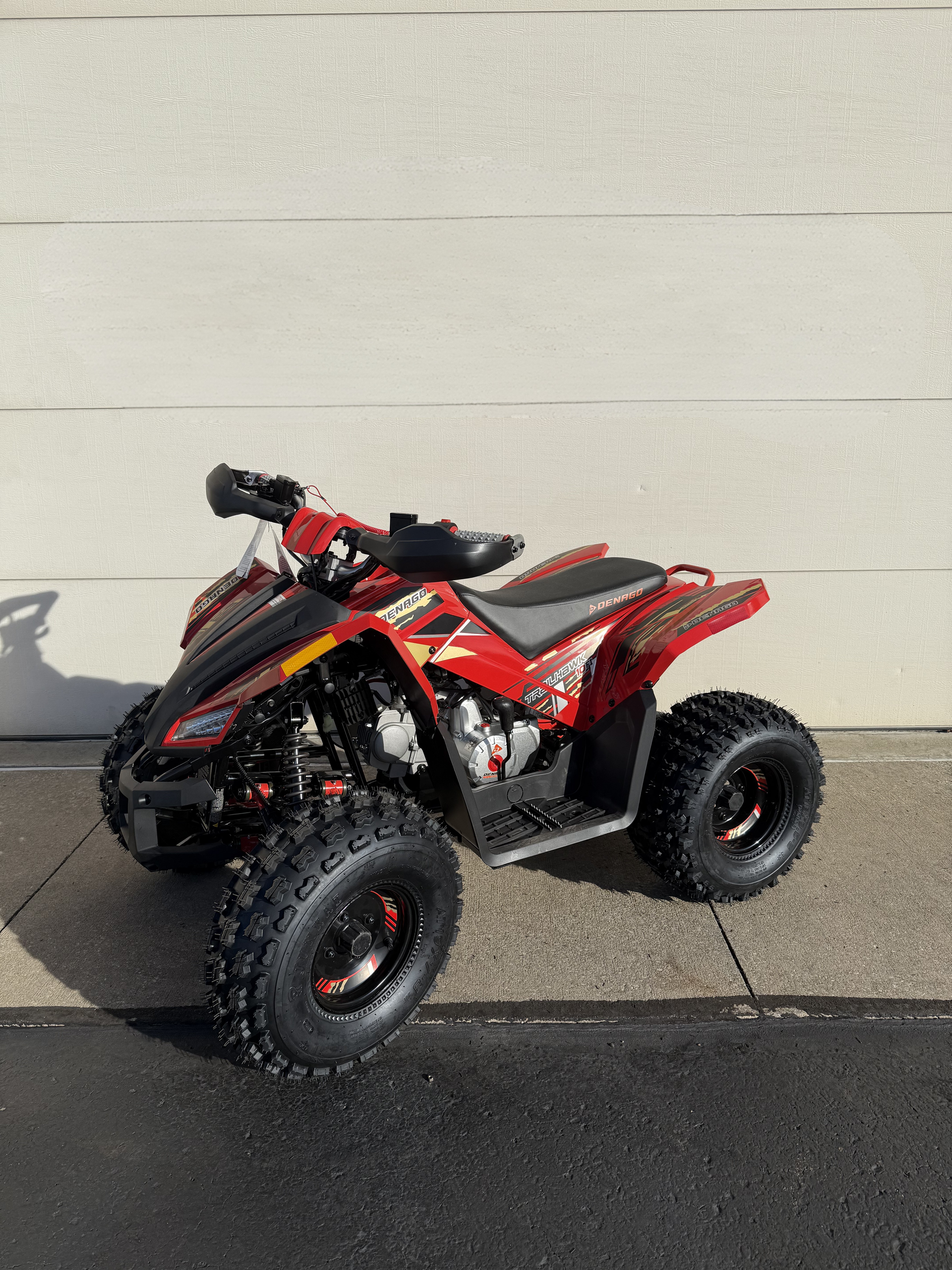 A red Polaris youth ATV parked on a paved surface against a plain light wall.