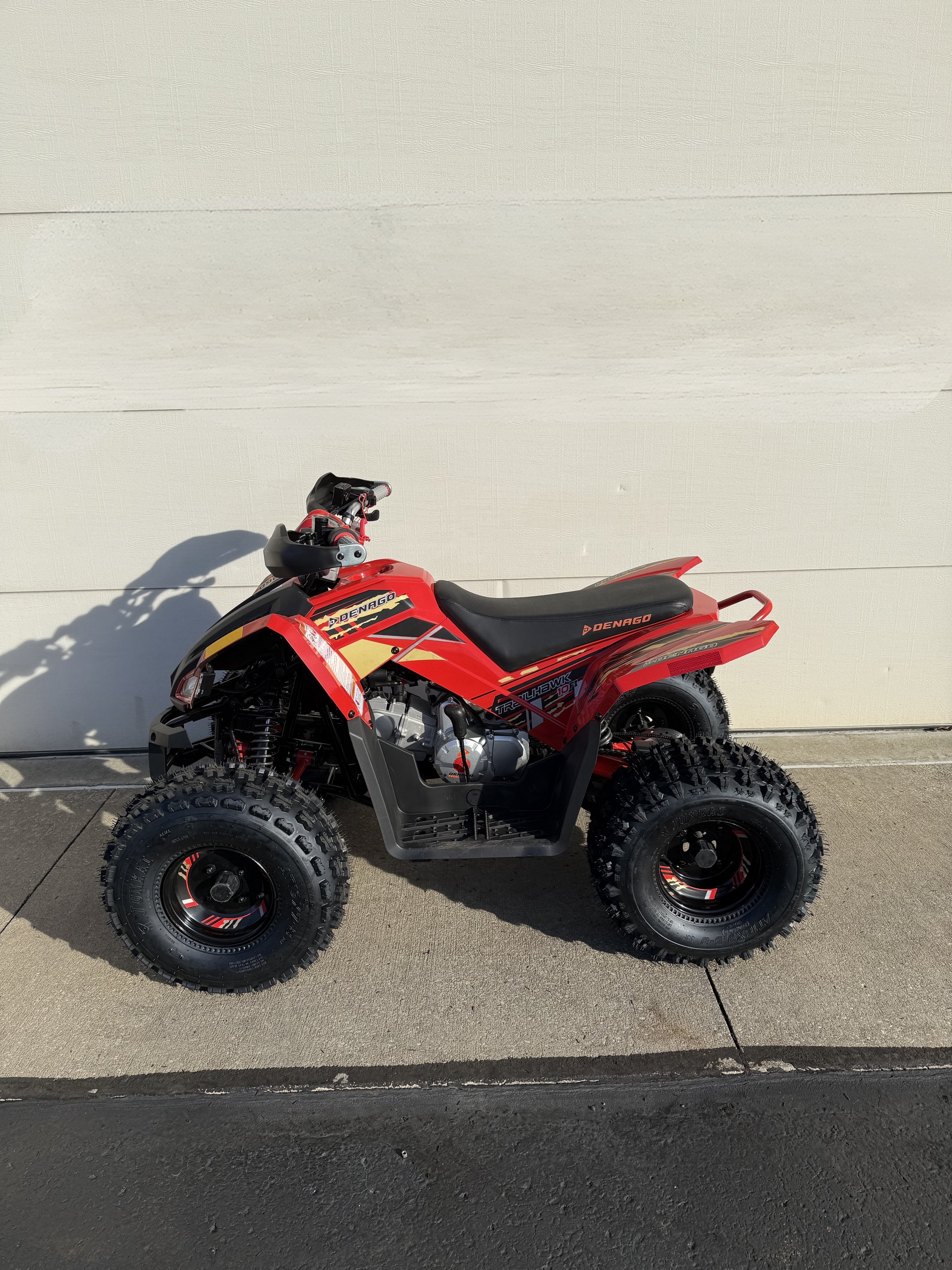 A red youth-sized ATV parked on concrete in front of a plain white wall.