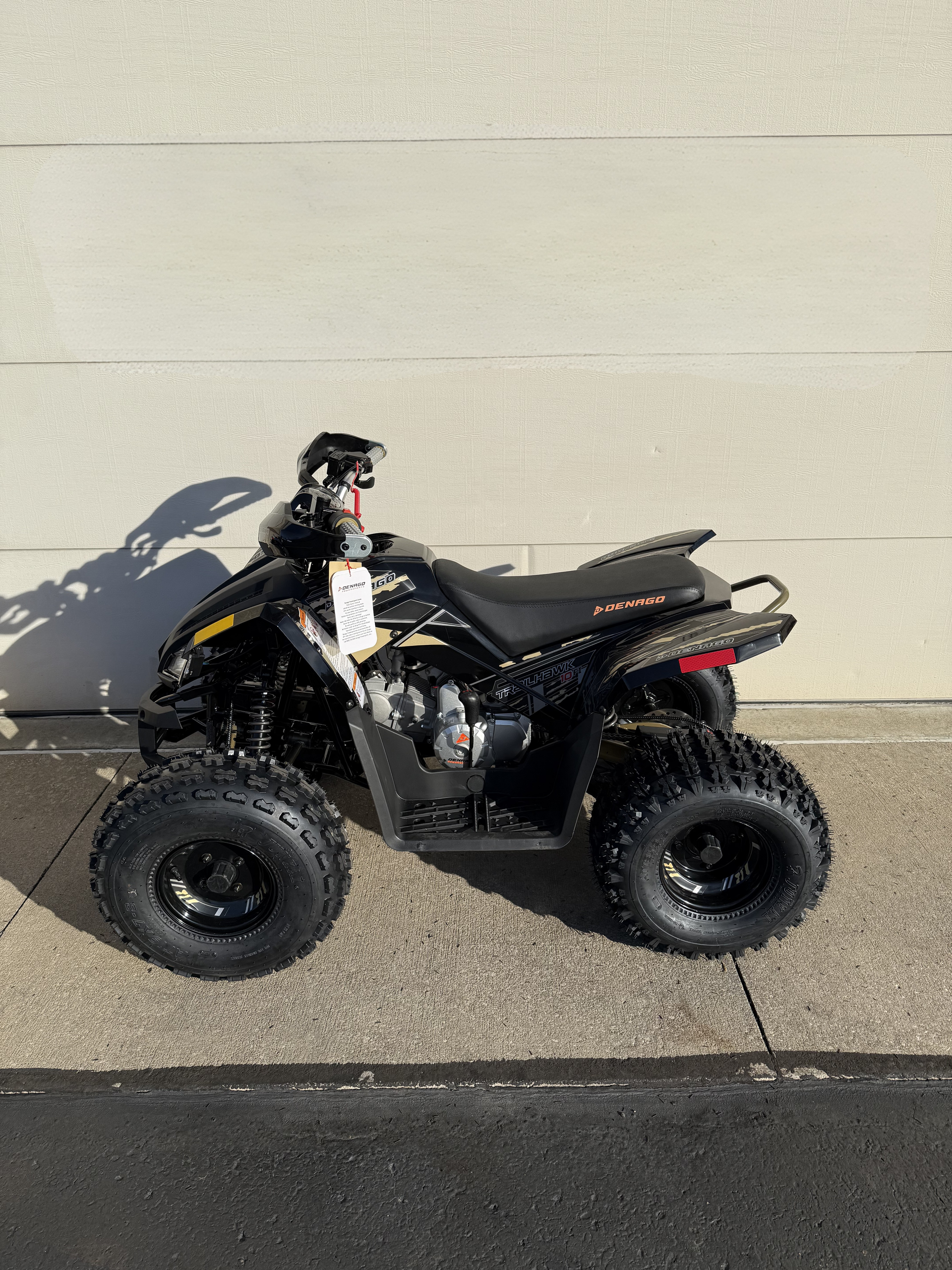 A black all-terrain vehicle (ATV) parked on a paved surface against a light-colored brick wall.