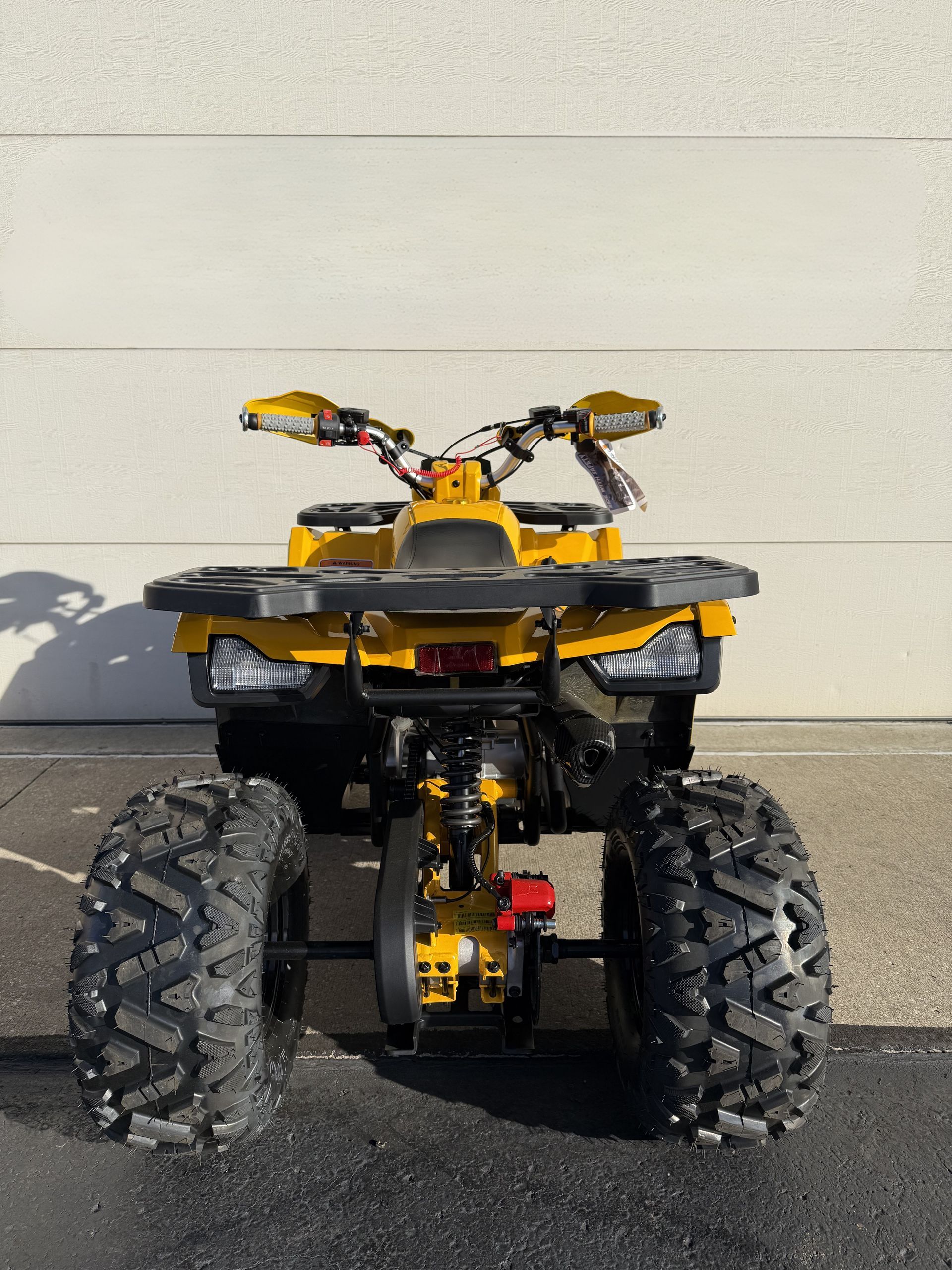 Rear view of a yellow all-terrain vehicle parked on asphalt against a white wall.