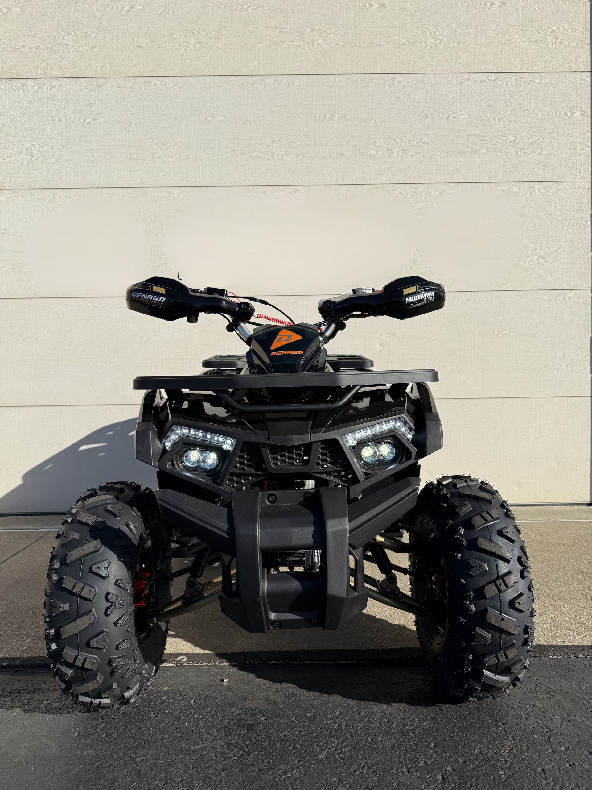 A black all-terrain vehicle (ATV) facing forward, parked on pavement against a white wall.