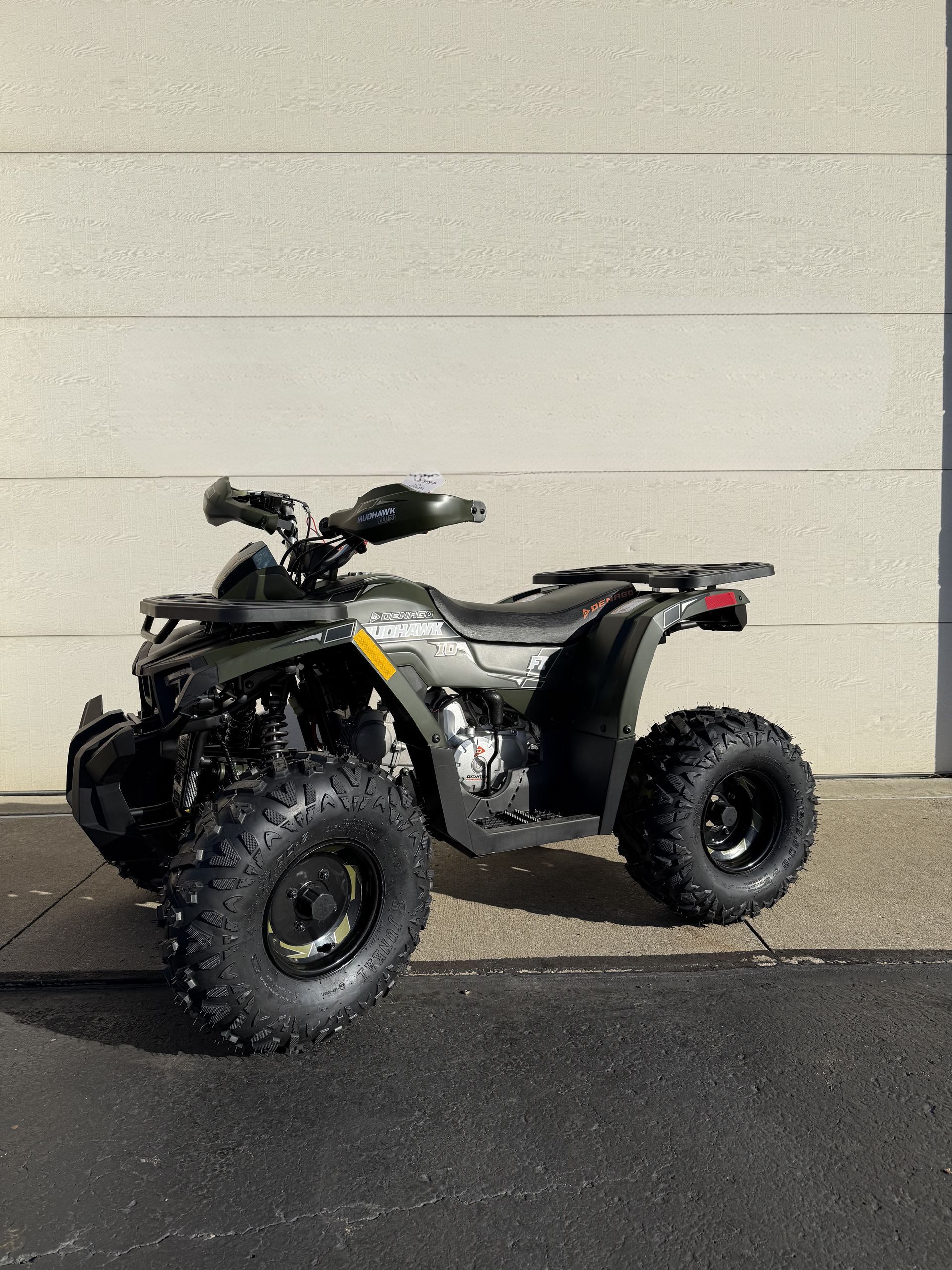 A dark green all-terrain vehicle (ATV) parked on pavement in front of a white wall.