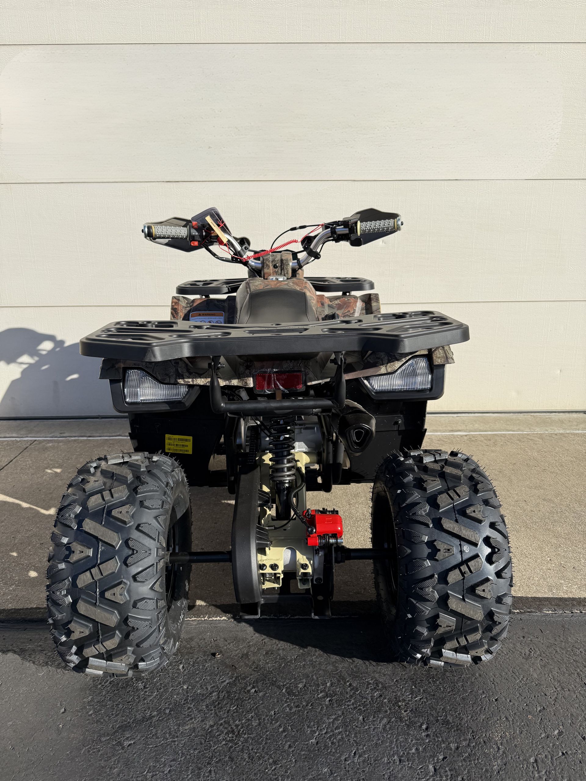 Rear view of a camouflage-patterned ATV parked on asphalt in front of a white wall.