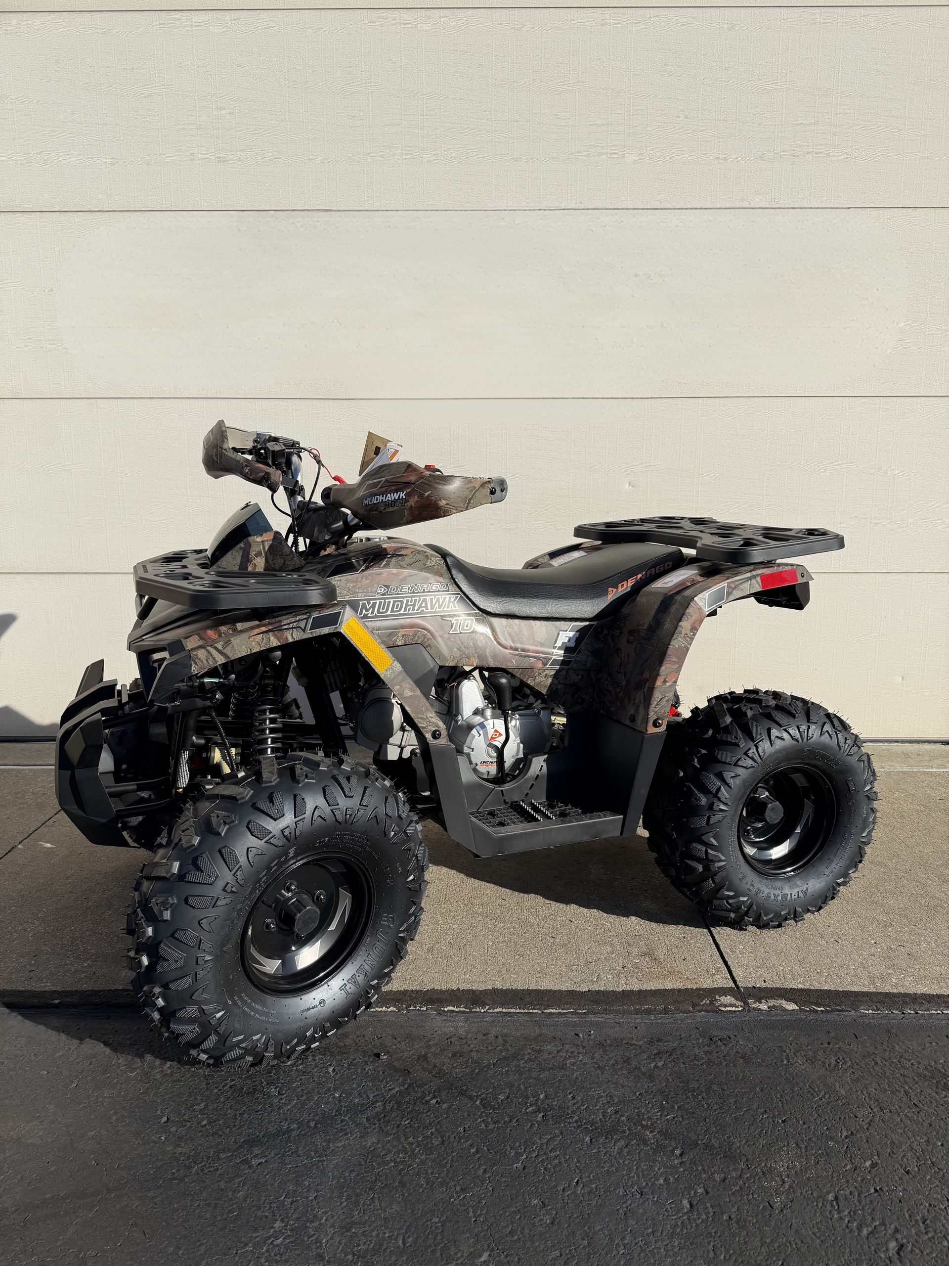A camouflage-patterned ATV parked on a paved surface against a neutral concrete wall.