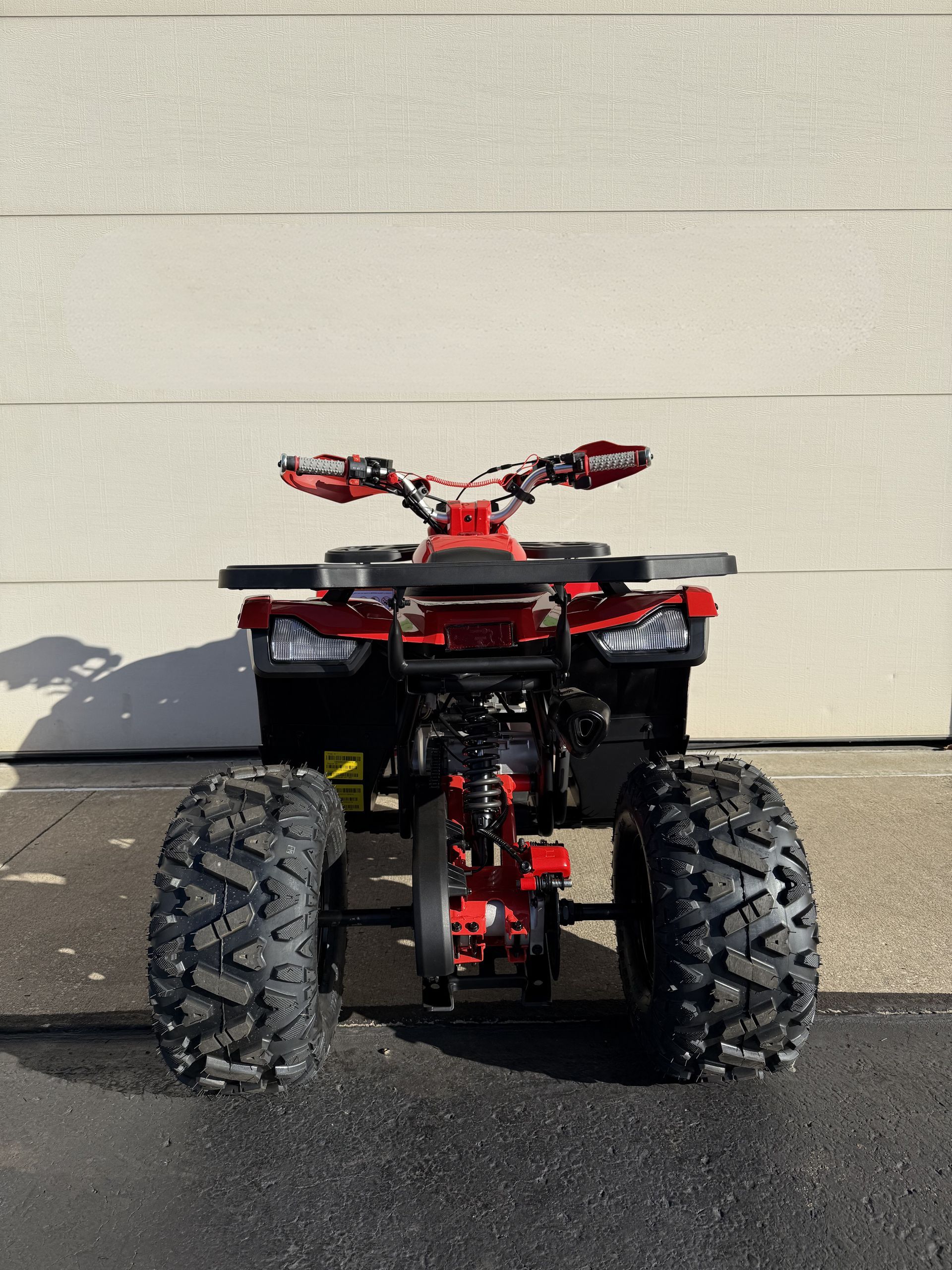 A red ATV viewed from the rear, parked on asphalt in front of a light-colored garage door.