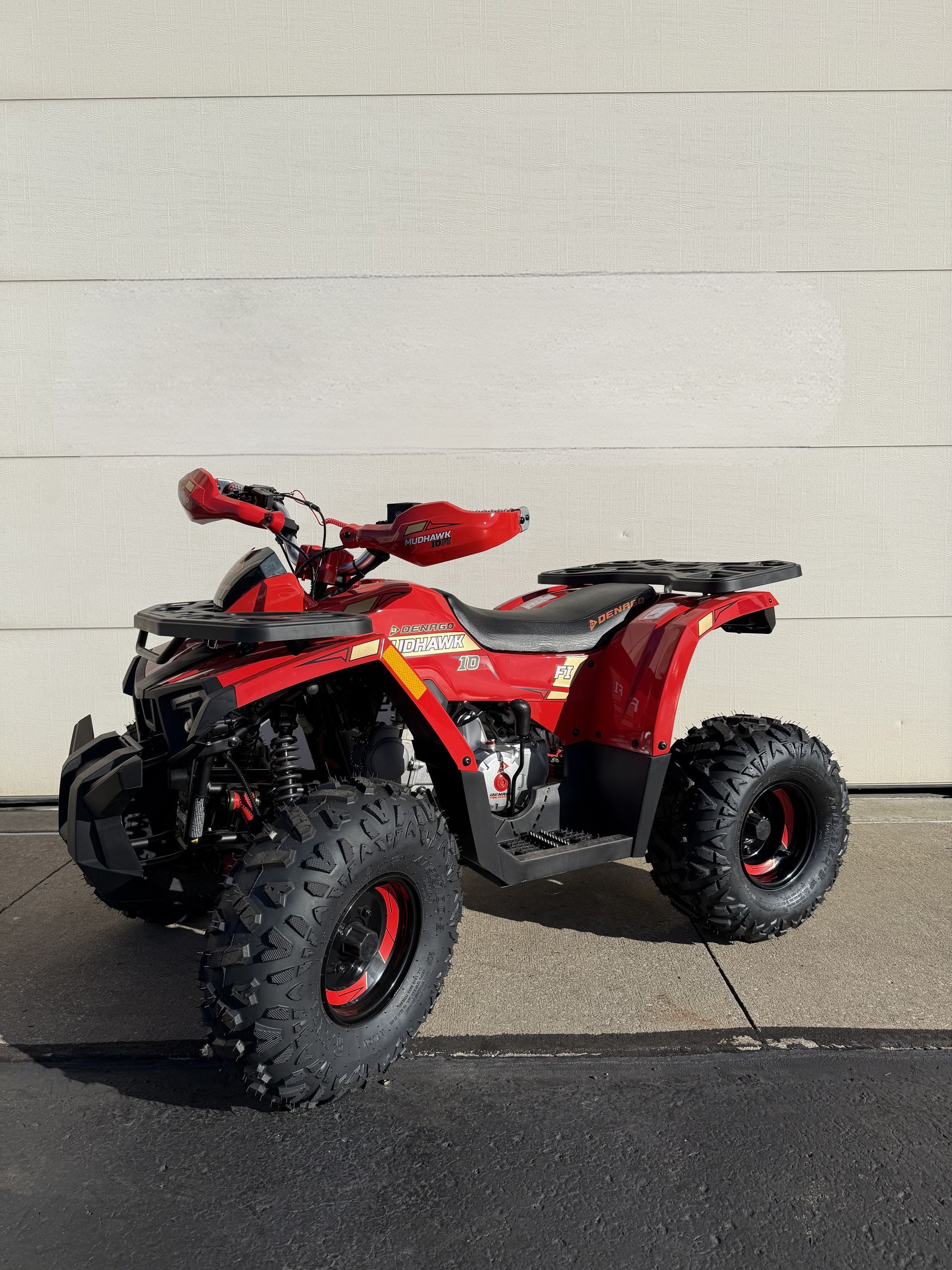 A red ATV with black tires parked on asphalt in front of a white wall.