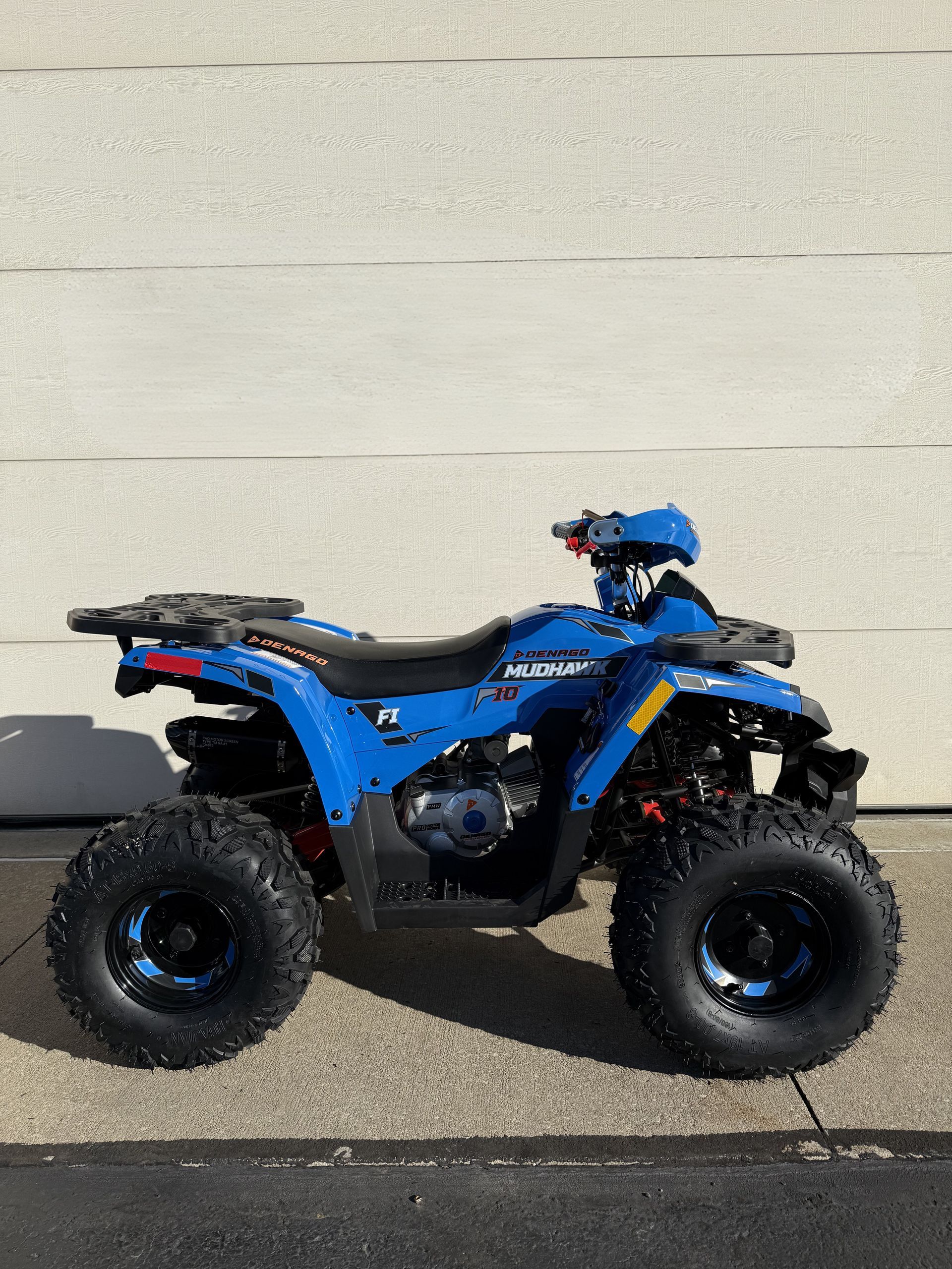 A bright blue ATV parked on a concrete surface against a beige wall.