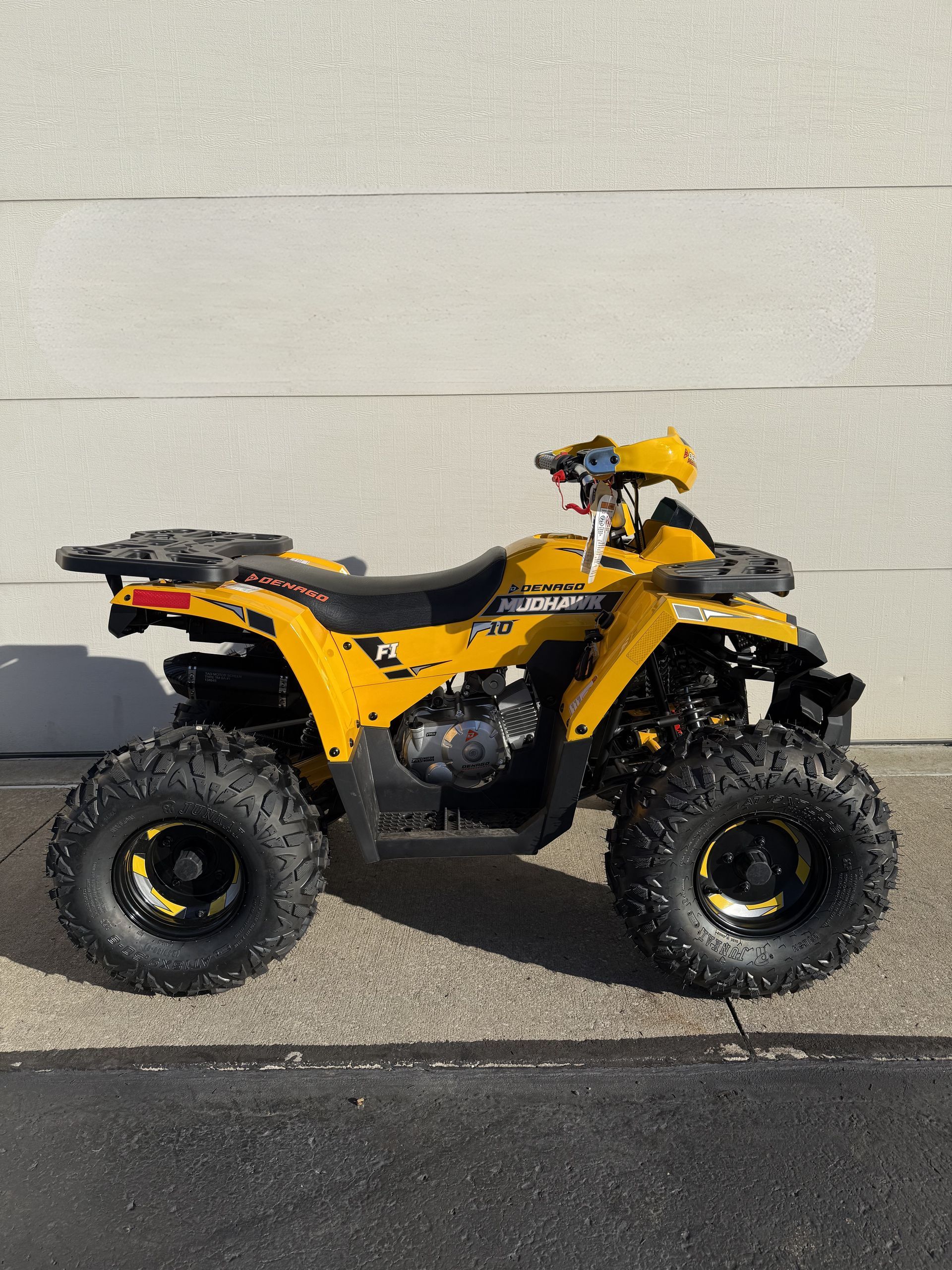 A yellow all-terrain vehicle parked on asphalt against a light-colored wall.