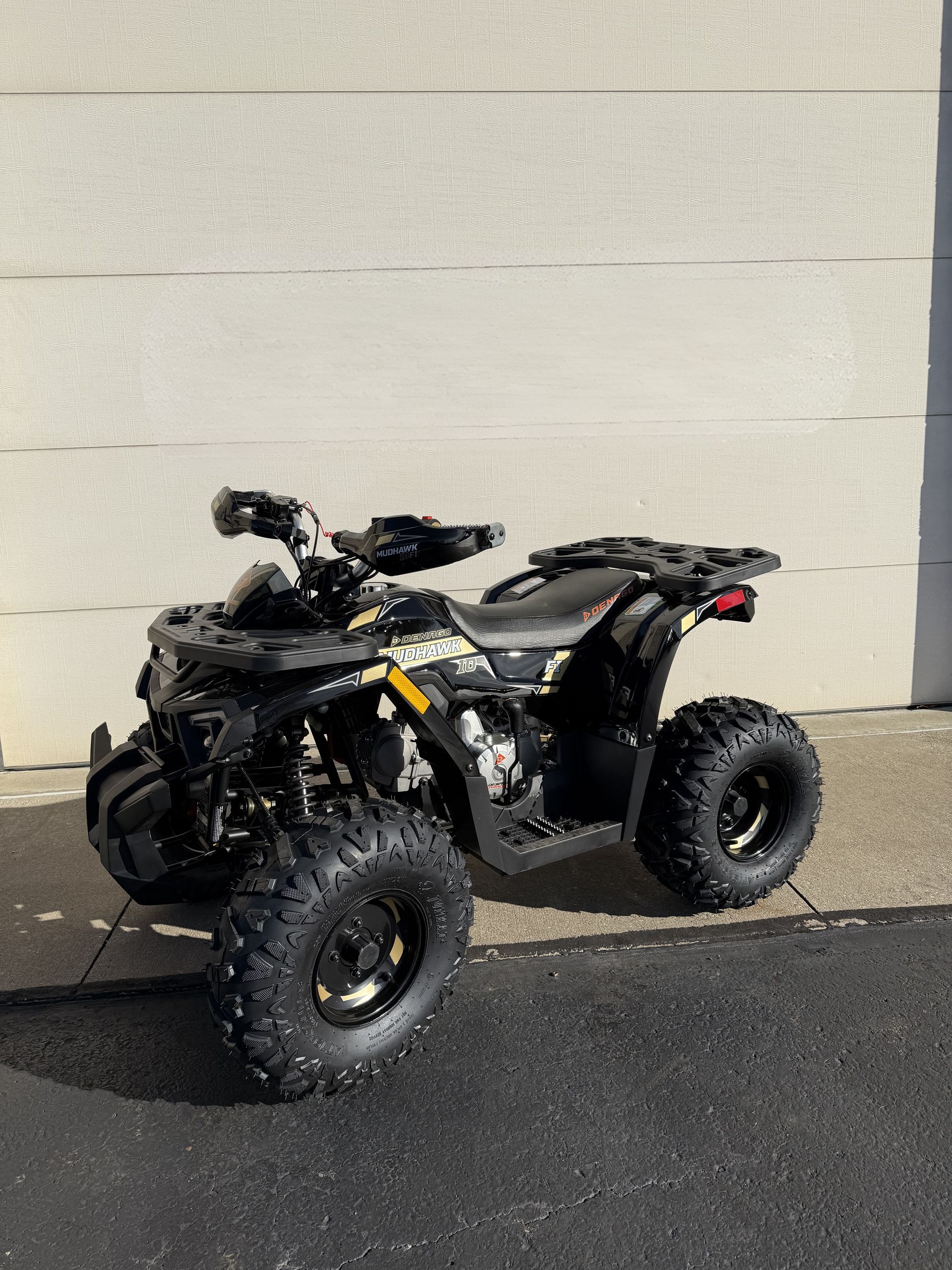 A black and yellow Polaris ATV parked outdoors against a light-colored wall.
