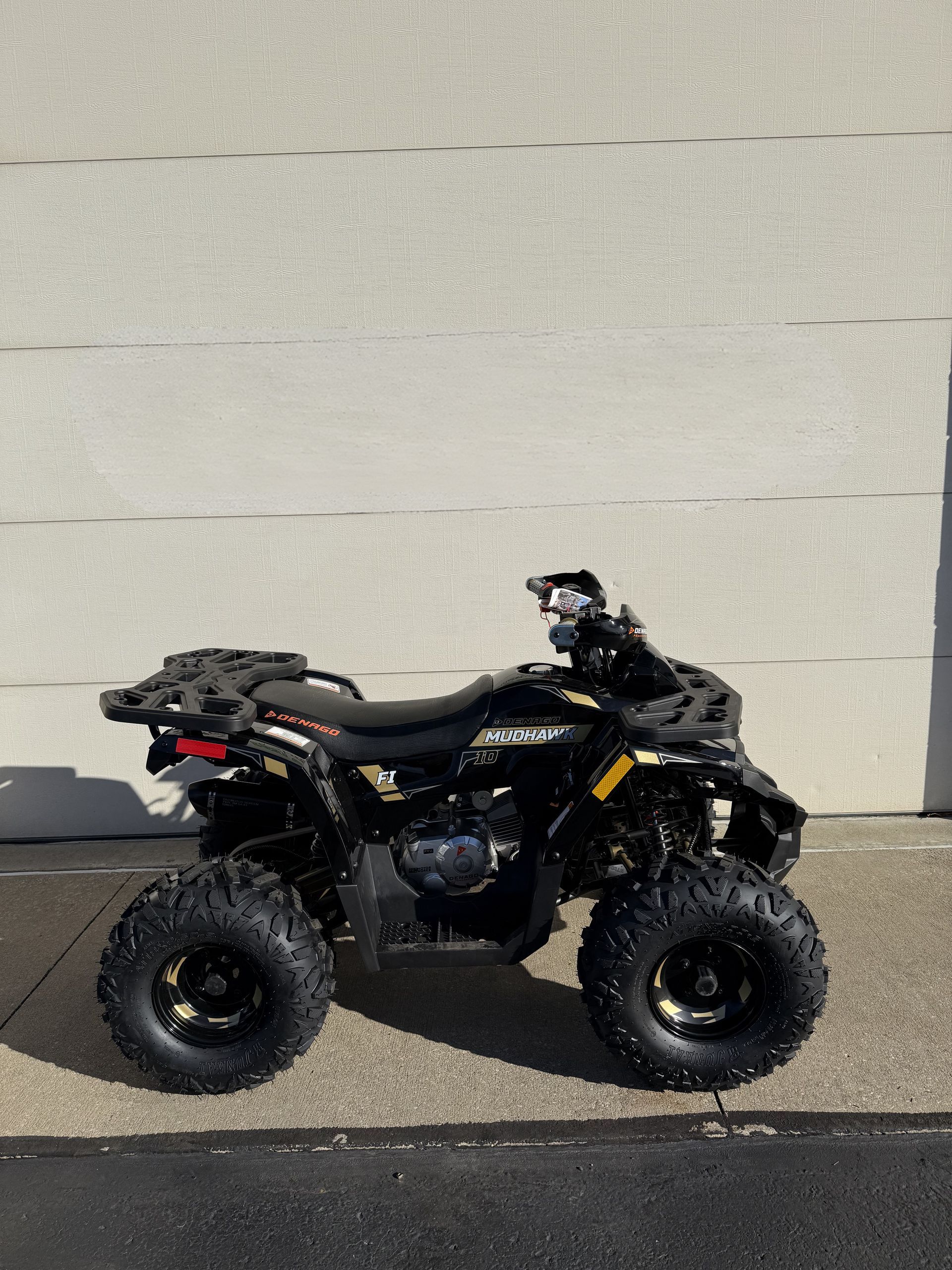 A black all-terrain vehicle (ATV) parked outdoors on asphalt in front of a light-colored building wall.