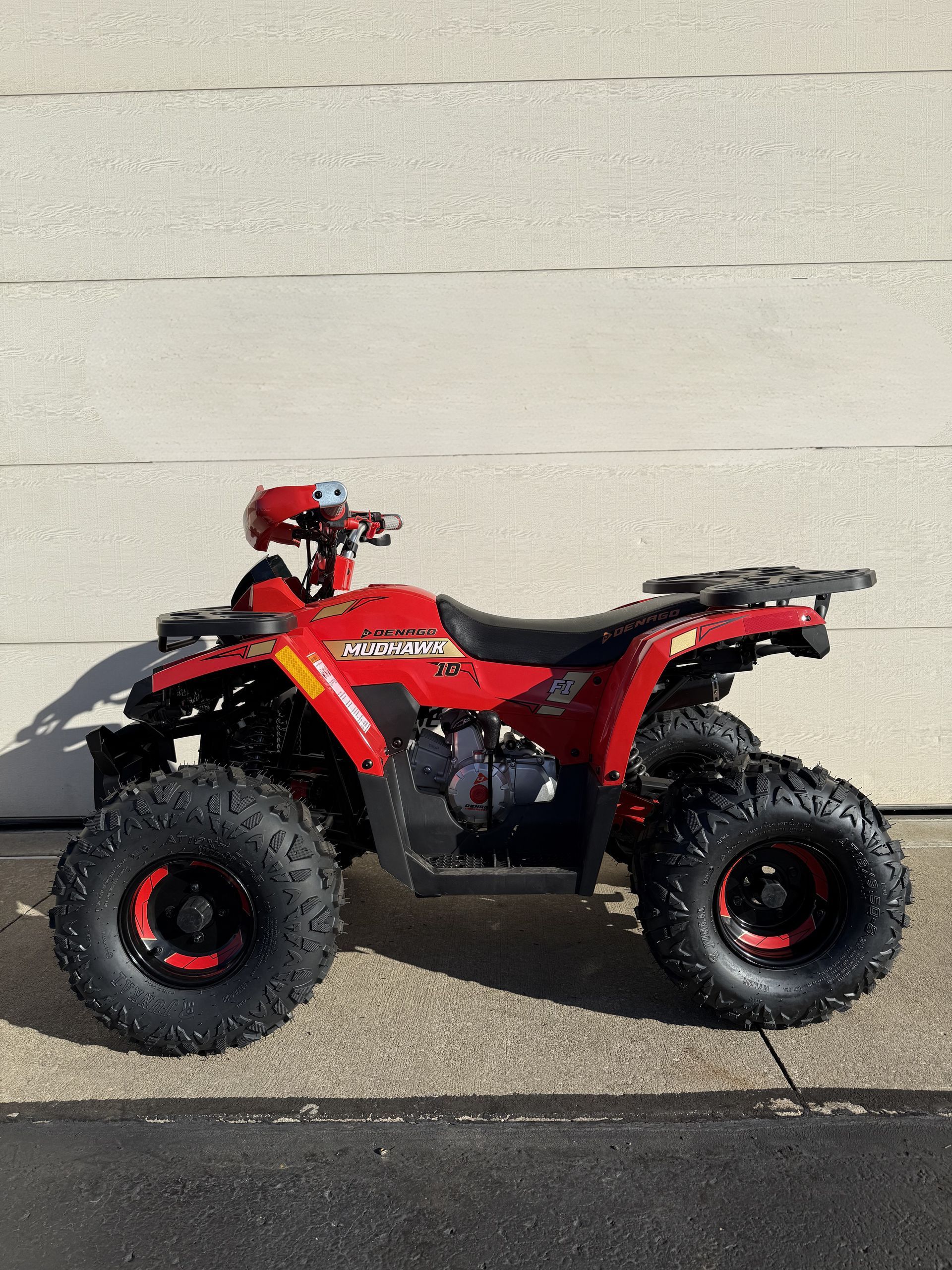 A red, single-rider ATV parked on pavement in front of a light-colored wall.