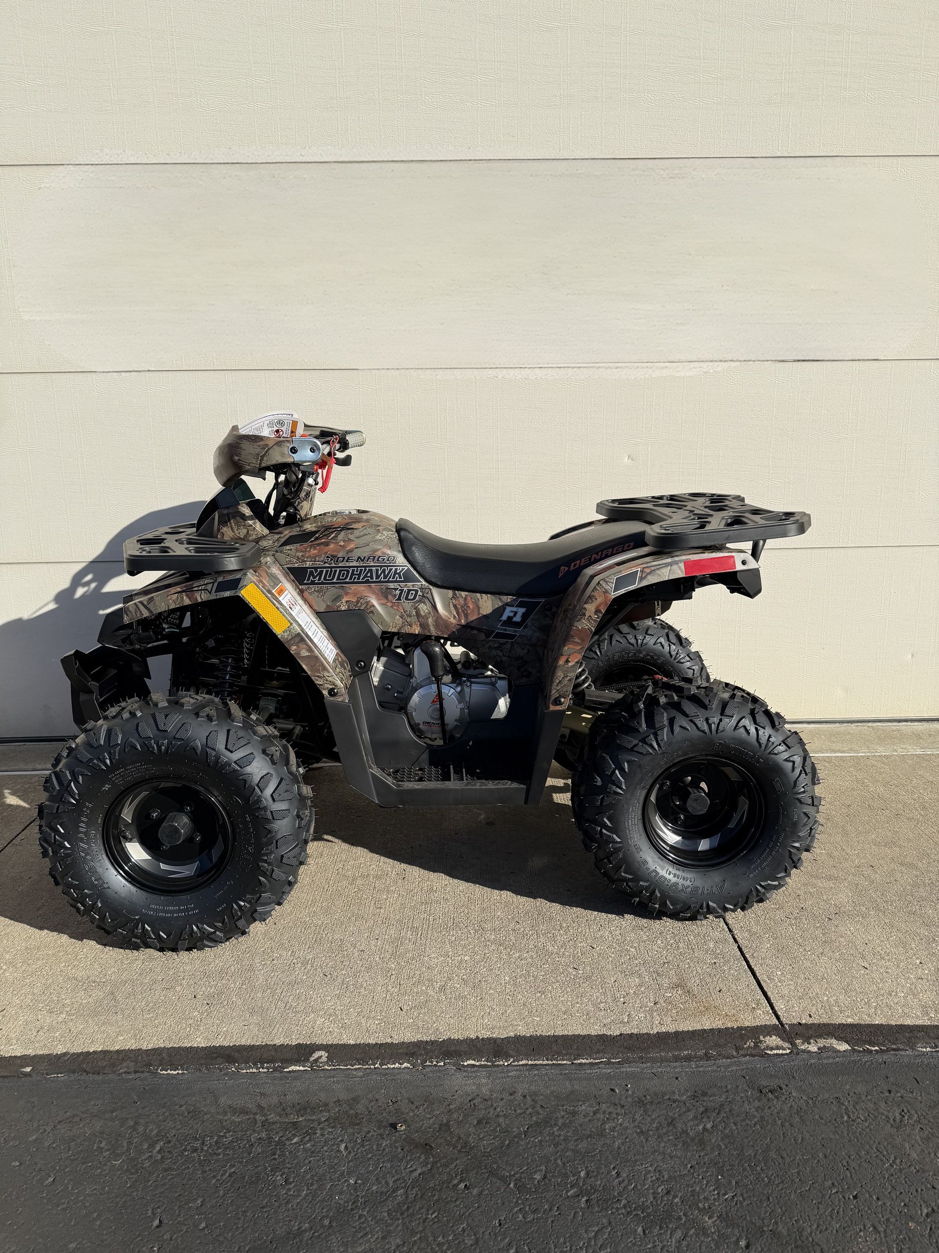 A side-profile view of a camouflage-patterned Polaris ATV parked on a concrete surface against a light-colored wall.