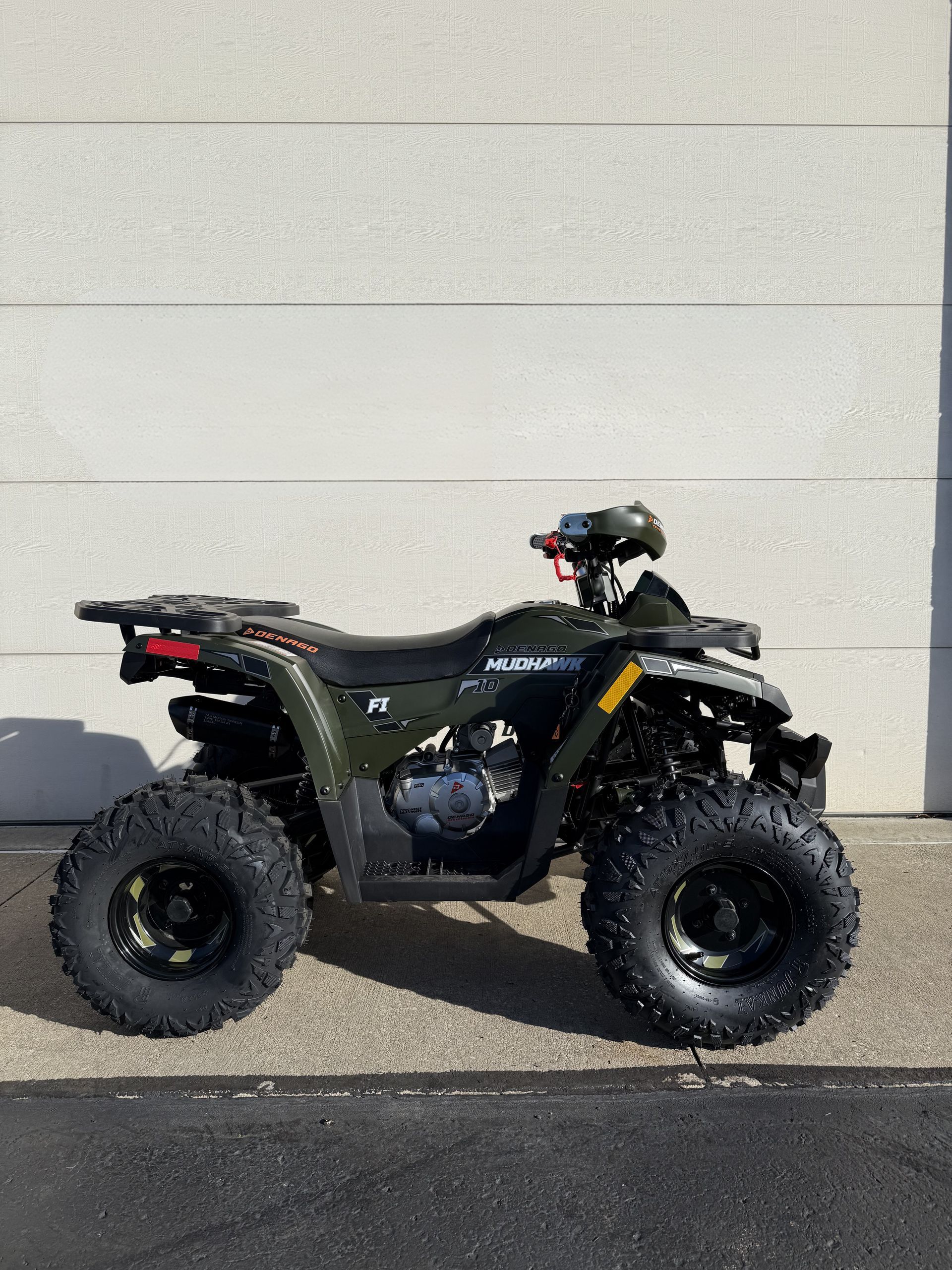 A dark green all-terrain vehicle (ATV) parked on a paved surface in front of a light-colored wall.