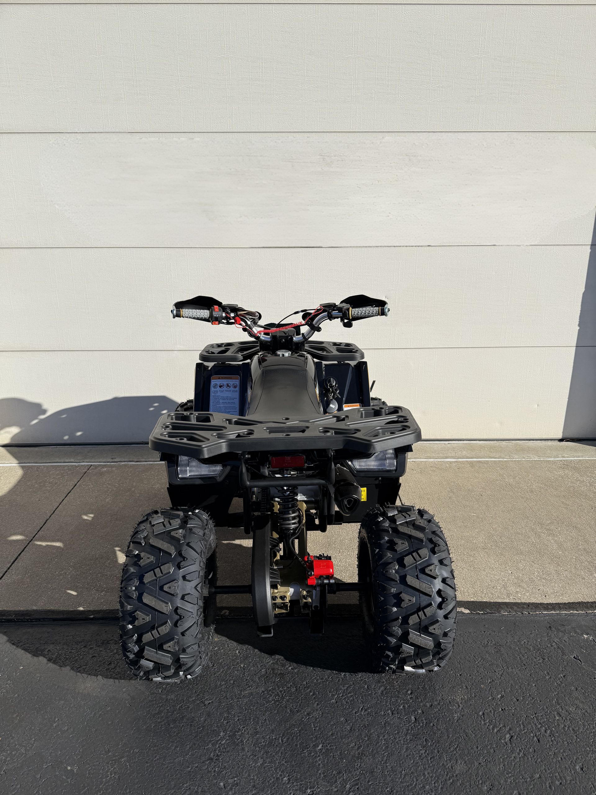A black ATV viewed from the rear, parked on pavement against a white wall.
