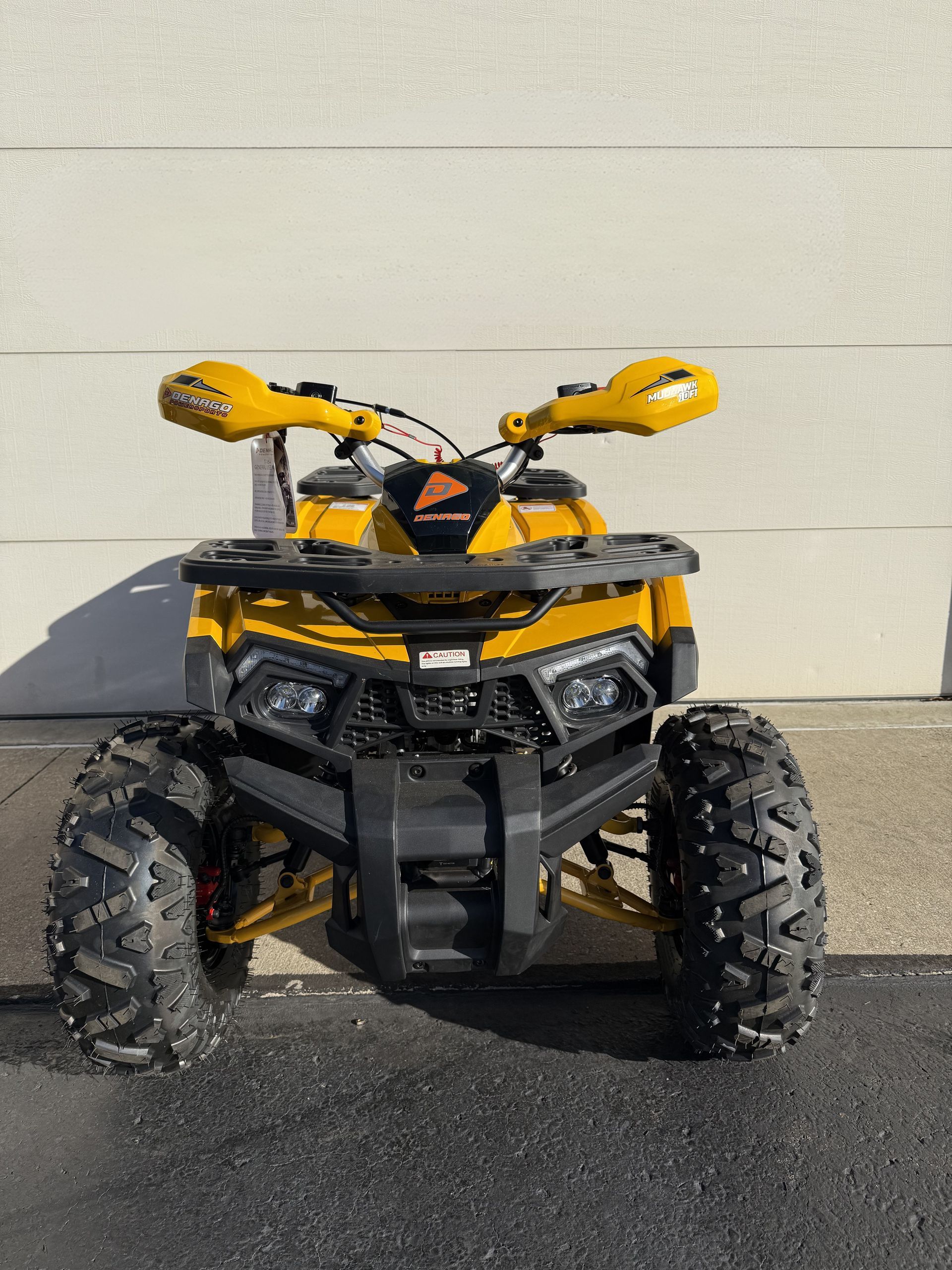 A bright yellow all-terrain vehicle (ATV) parked outdoors against a plain, light-colored wall.
