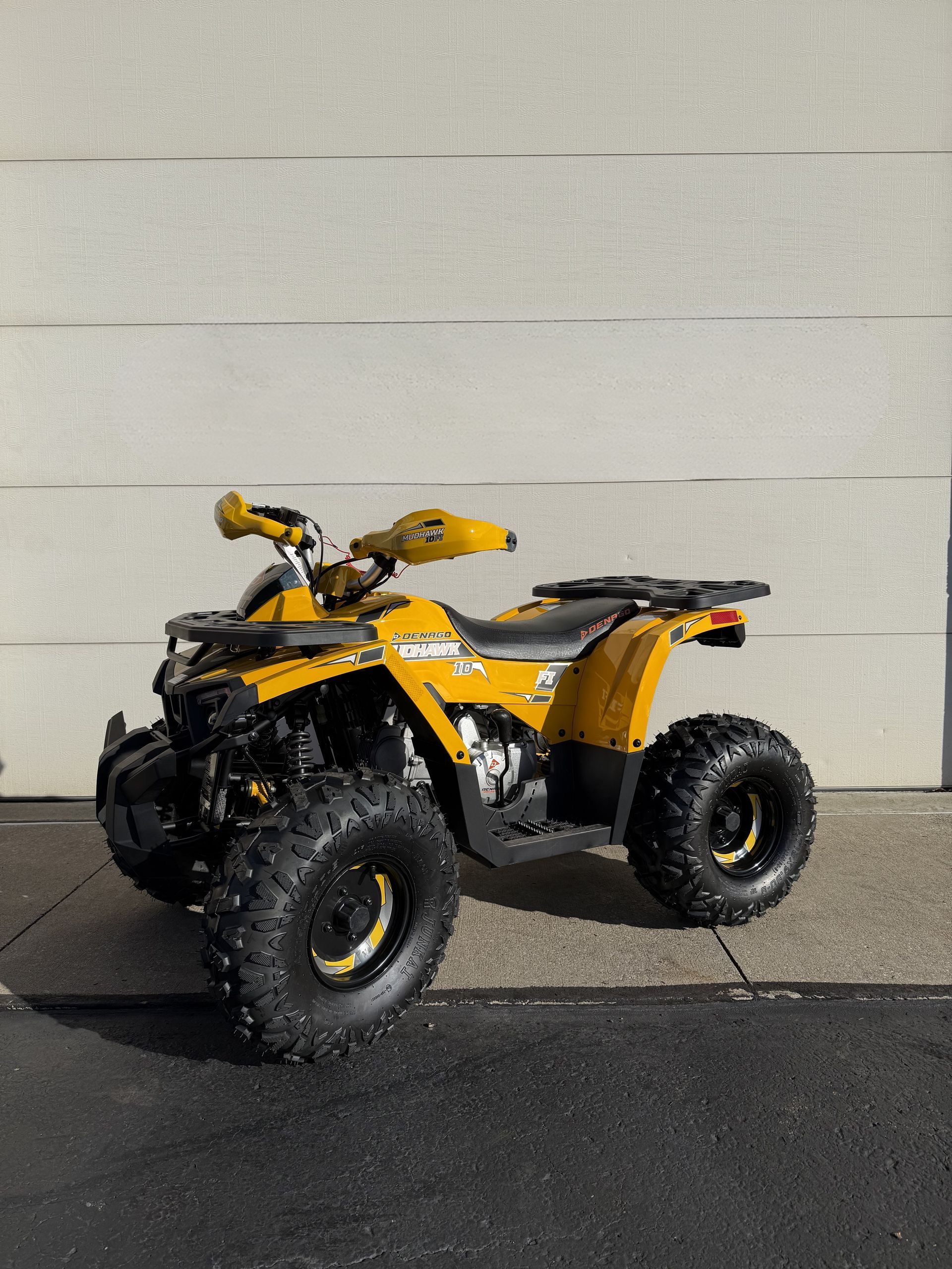 A yellow all-terrain vehicle (ATV) parked outdoors on a paved surface against a light-colored wall.