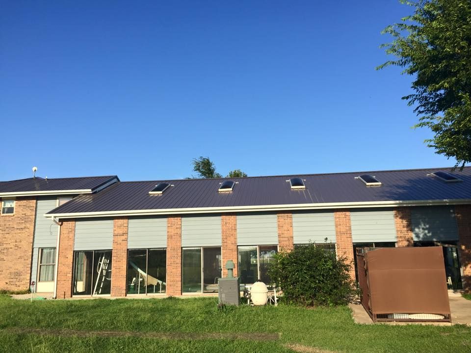 A two-story building with a new dark blue metal roof, glass doors, and brick accents against a blue sky.