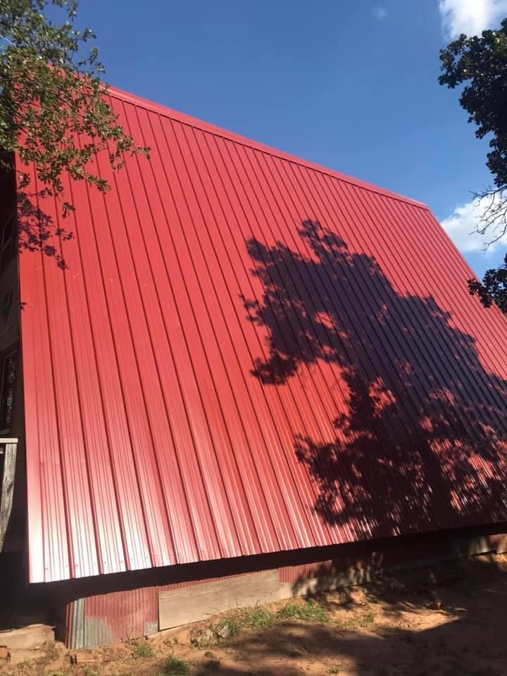 Red metal roof of a building with tree shadows on a sunny day.