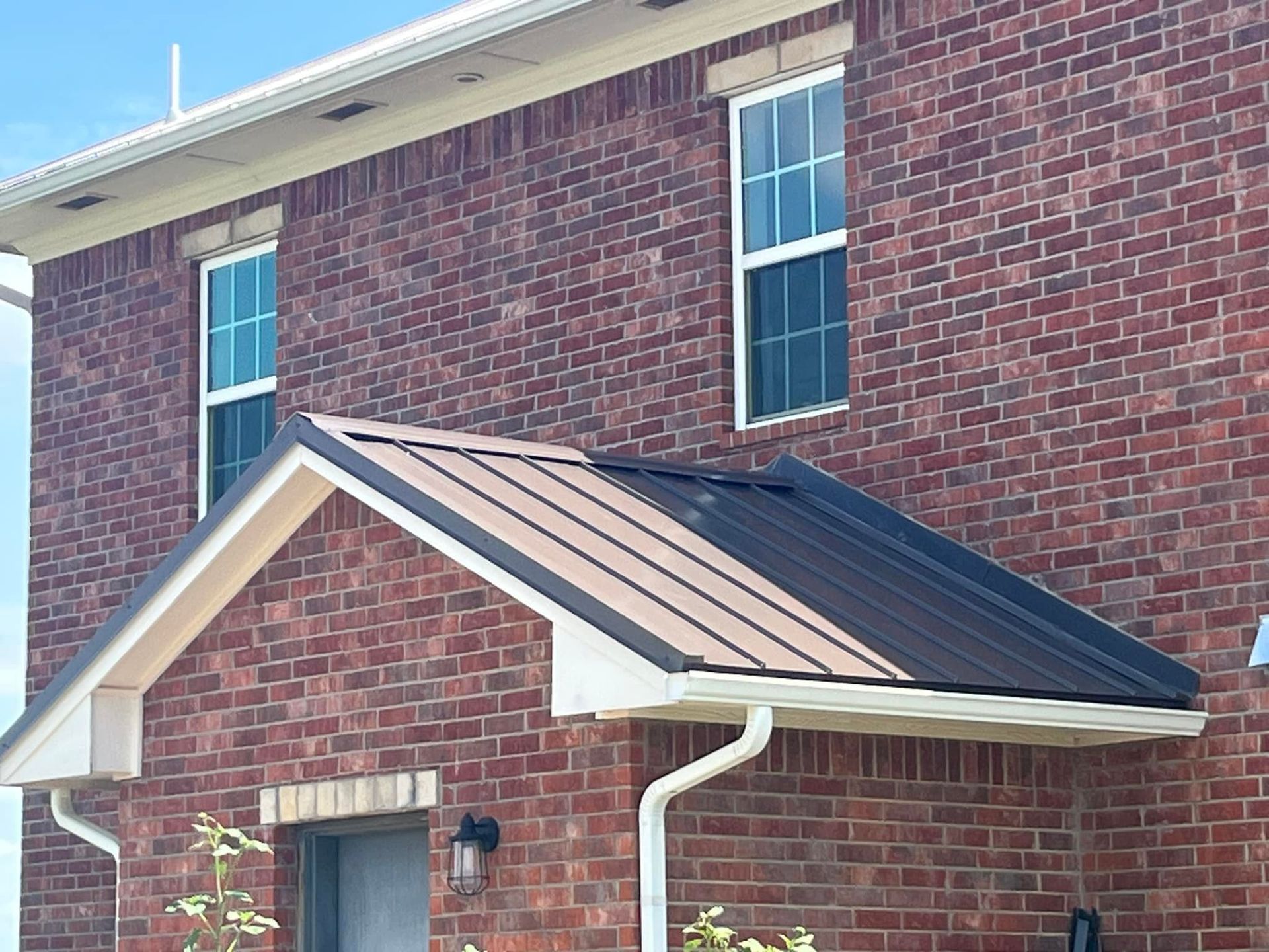 Brick building with metal roof awning, white trim, and windows; brown and white colors.