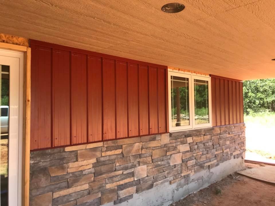 Red metal siding and stone wall on a house under a tan overhang.