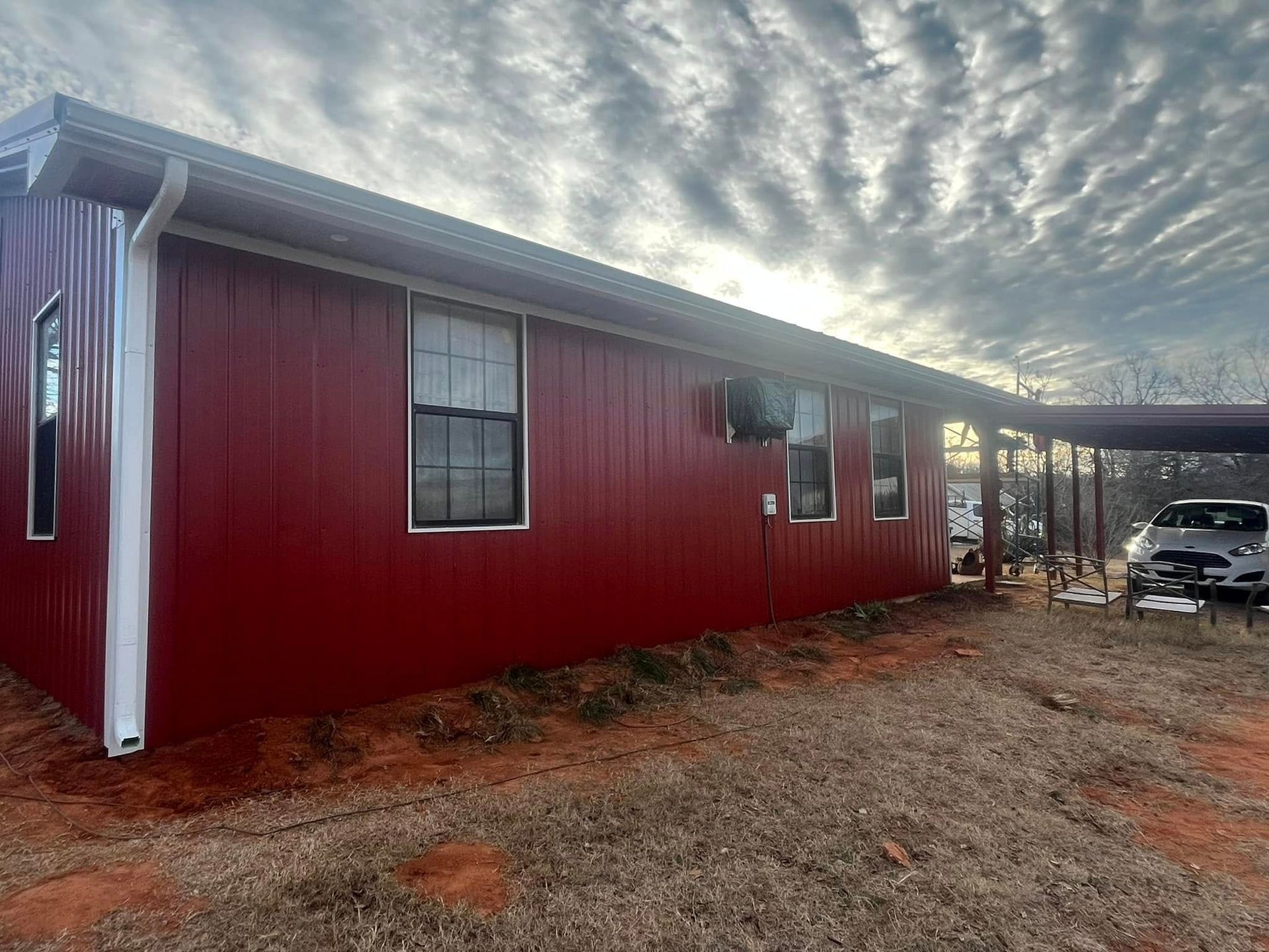 Red metal building with white trim, overcast sky, car under a carport.