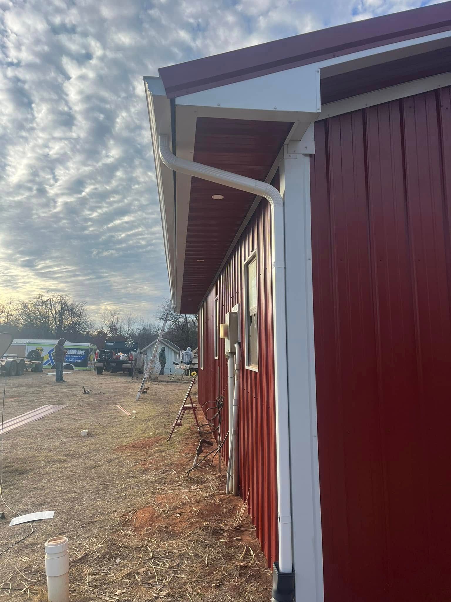 Red metal building with white trim and gutter against a cloudy sky.