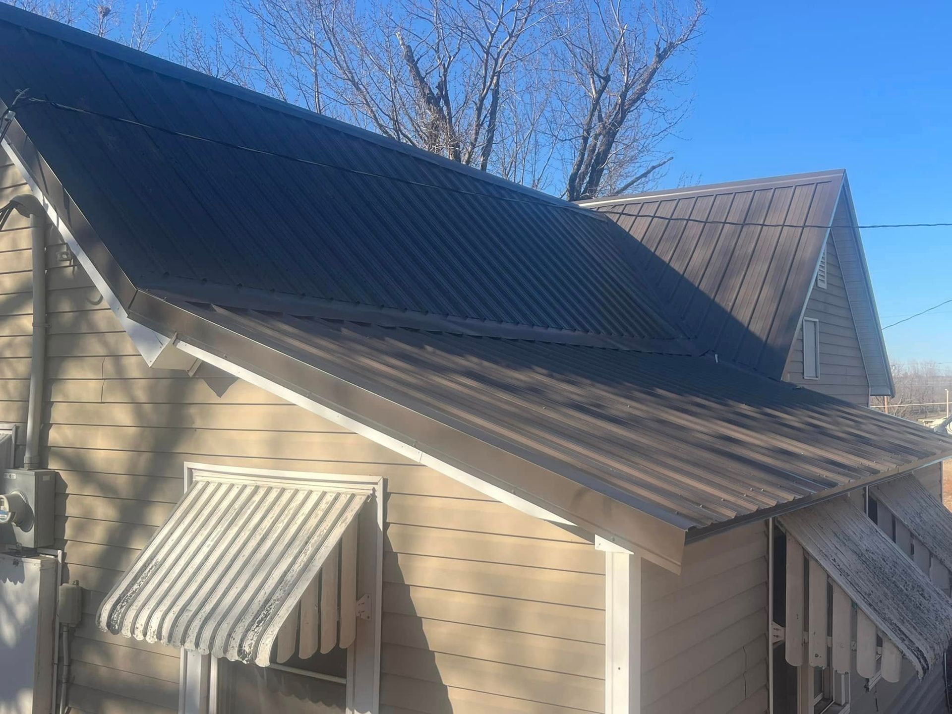 Brown metal roof on a tan house with white trim; awning visible under roof.