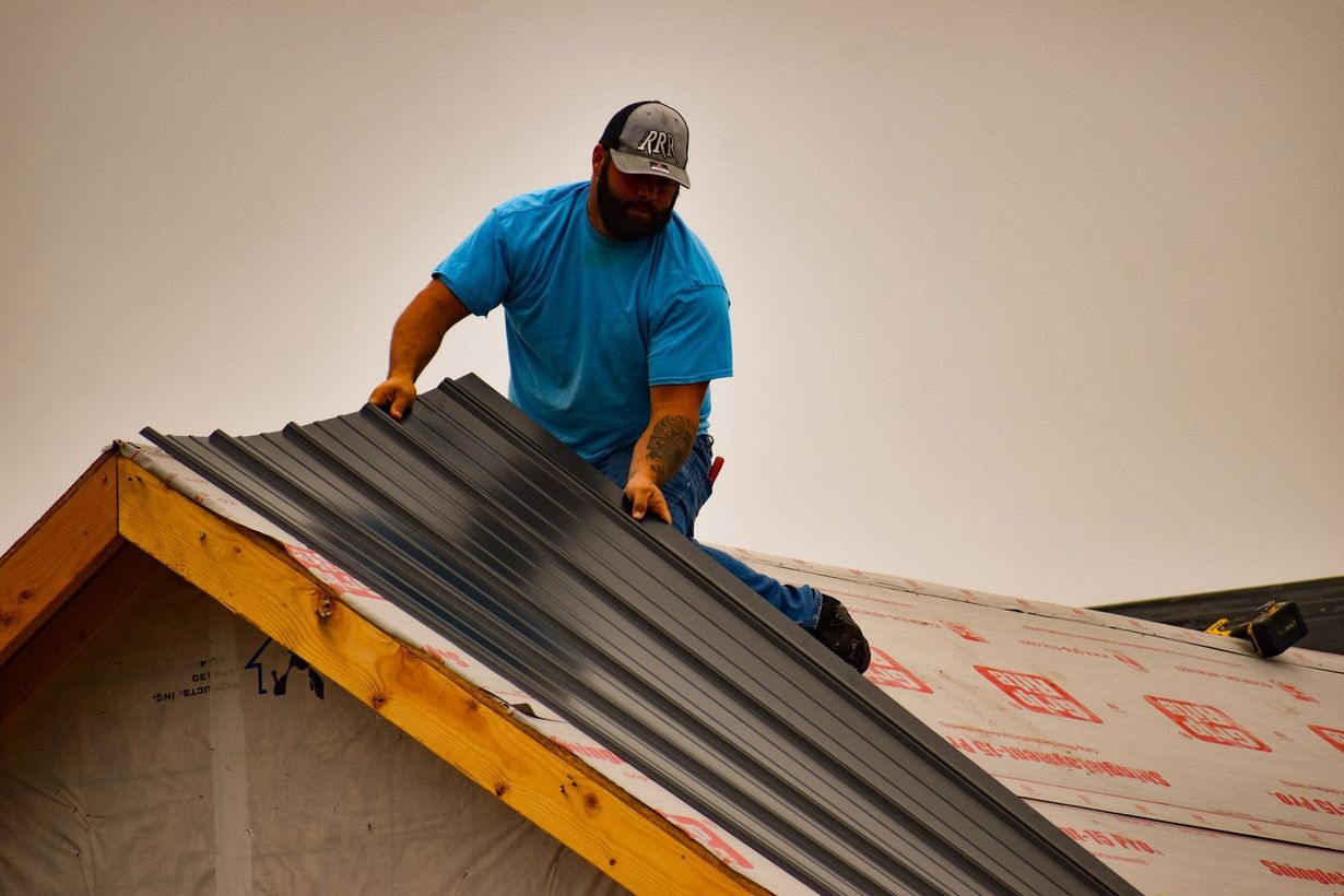 Man installing metal roofing on a wooden roof frame.