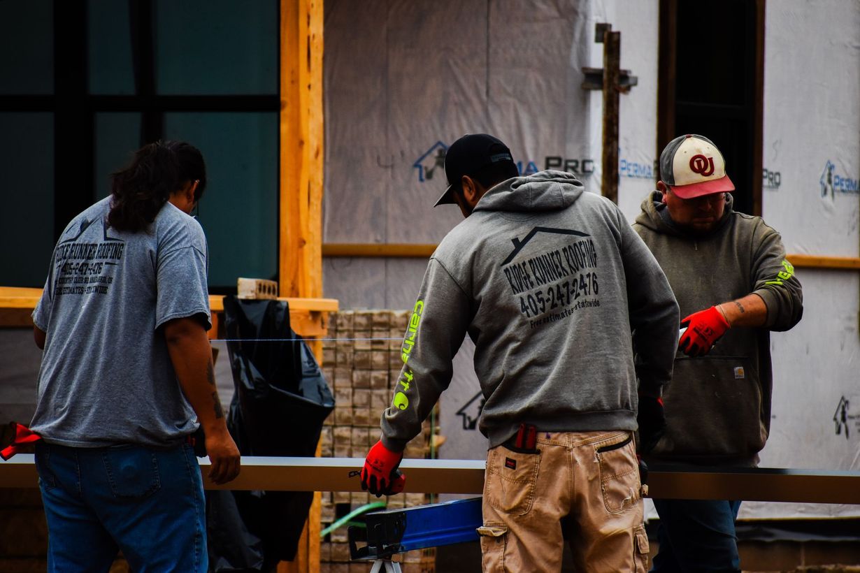 Three construction workers wearing gray shirts and caps, working on a building.