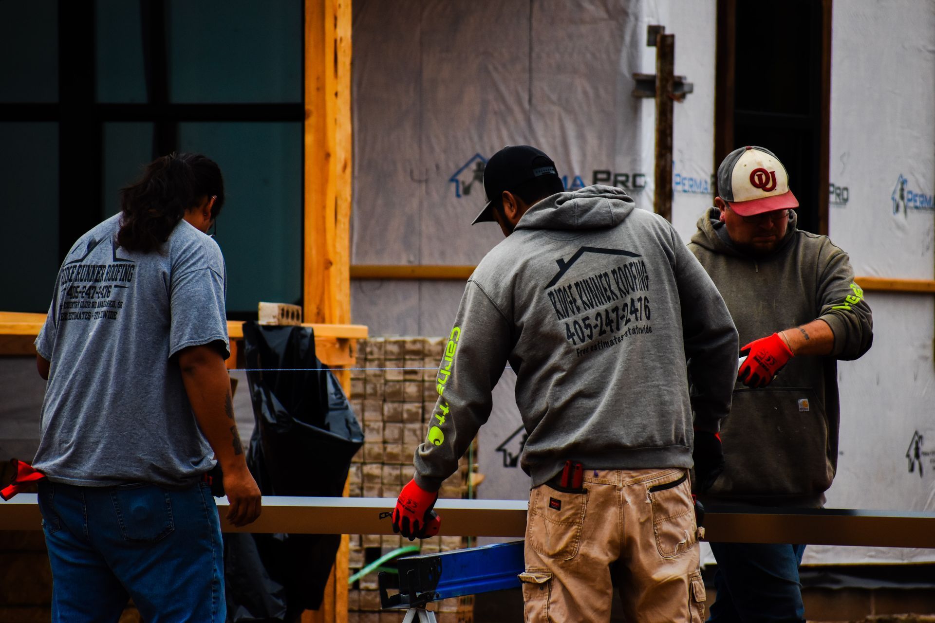 Three construction workers wearing gray shirts and caps, working on a building.
