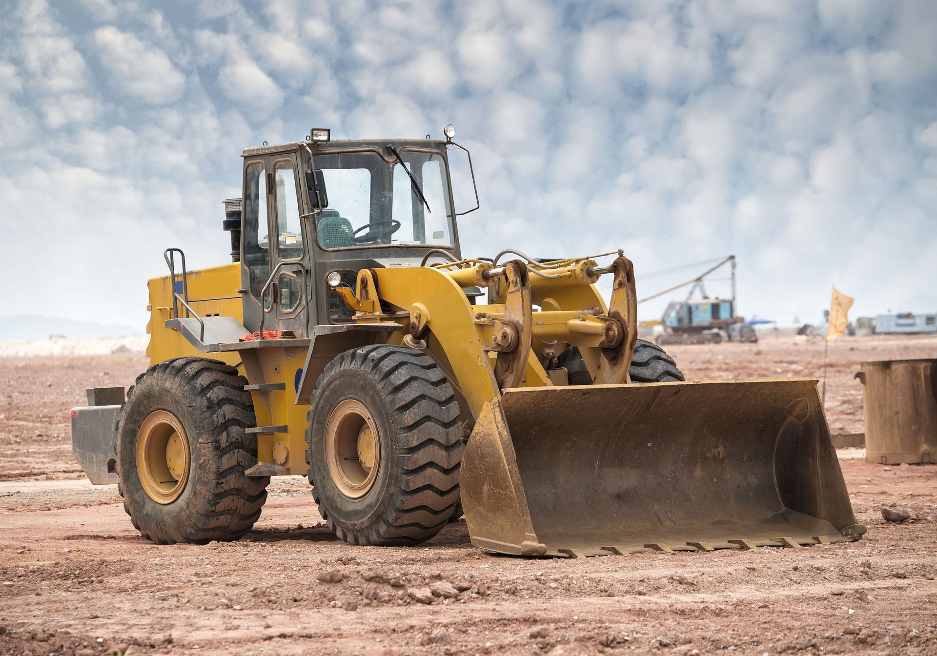 Yellow front-end loader on dirt in a construction site with blue cloudy sky in the background.