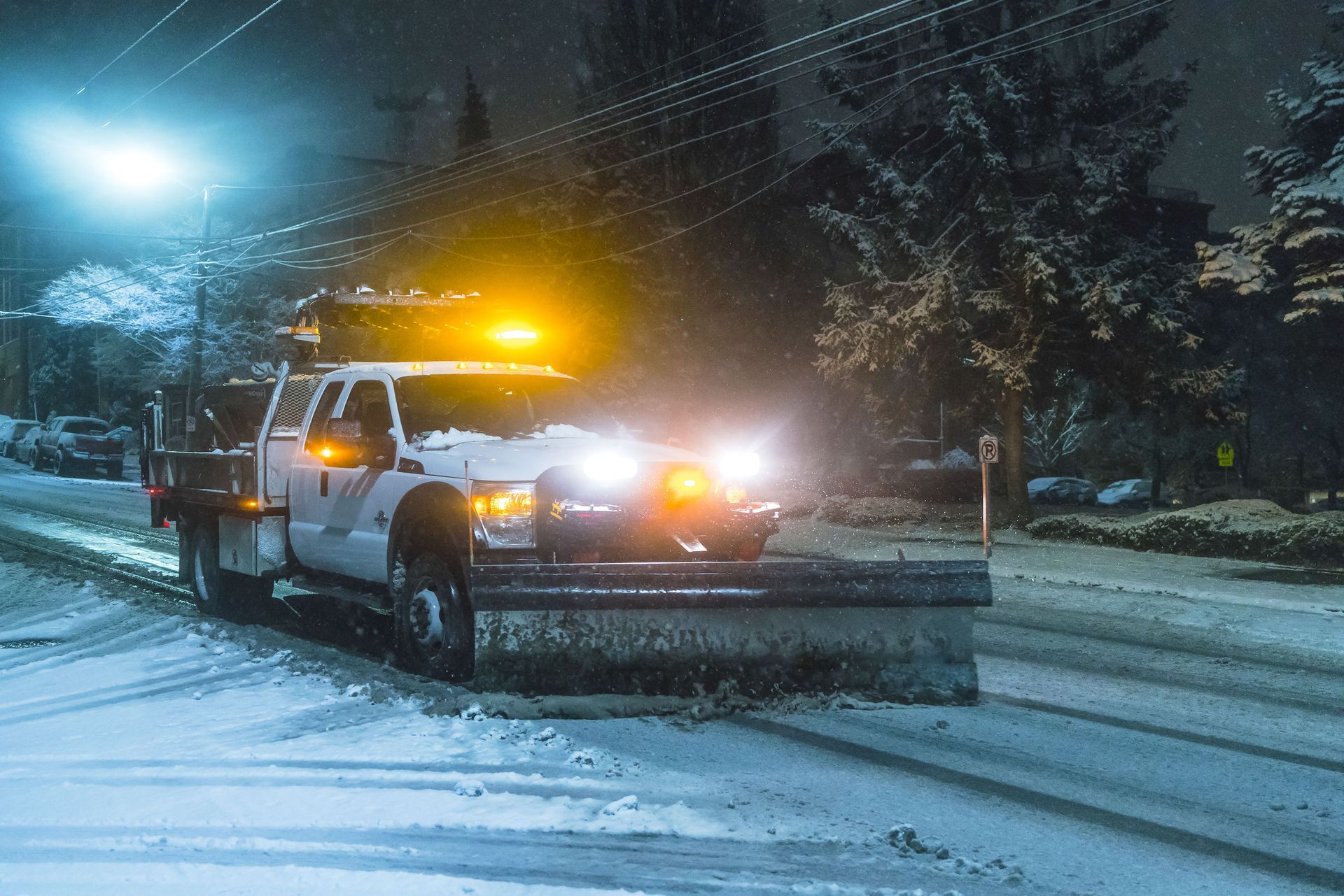 Snowplow clearing a snowy road at night, with flashing lights.