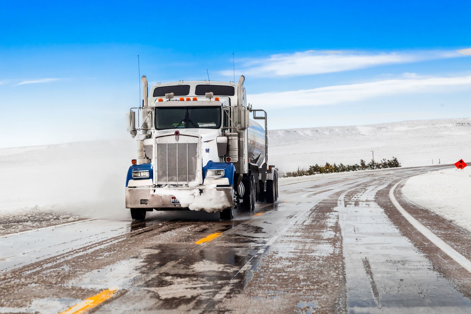Semi-truck on a snowy, icy road with a blue sky.