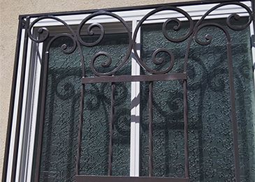 Decorative black wrought-iron window bars with scrollwork over a window.