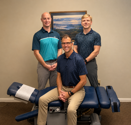 Three people pose in a clinic room beside a padded treatment table.
