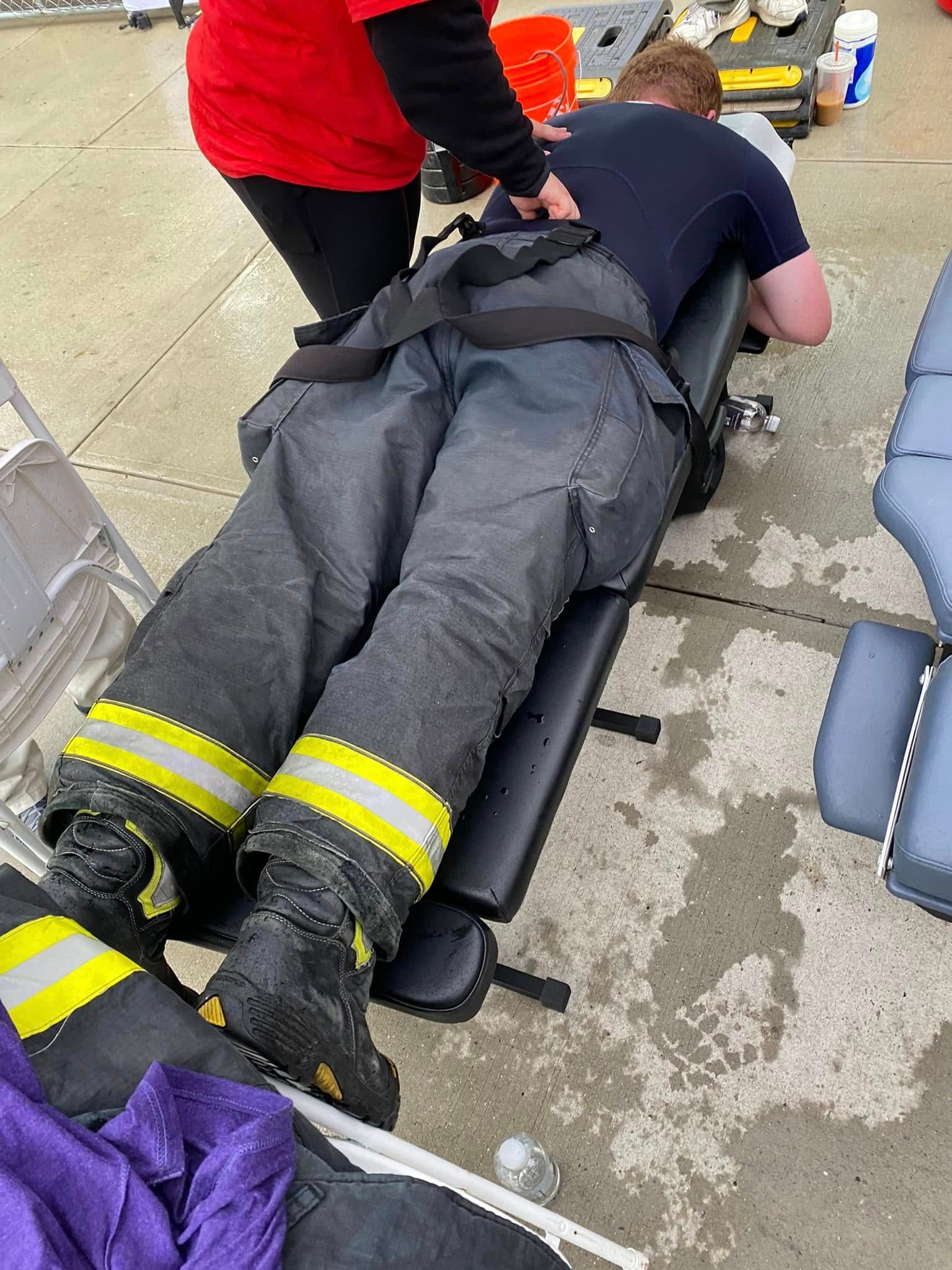 Paramedics attending an injured person lying on a stretcher on a wet sidewalk, with rescue gear nearby