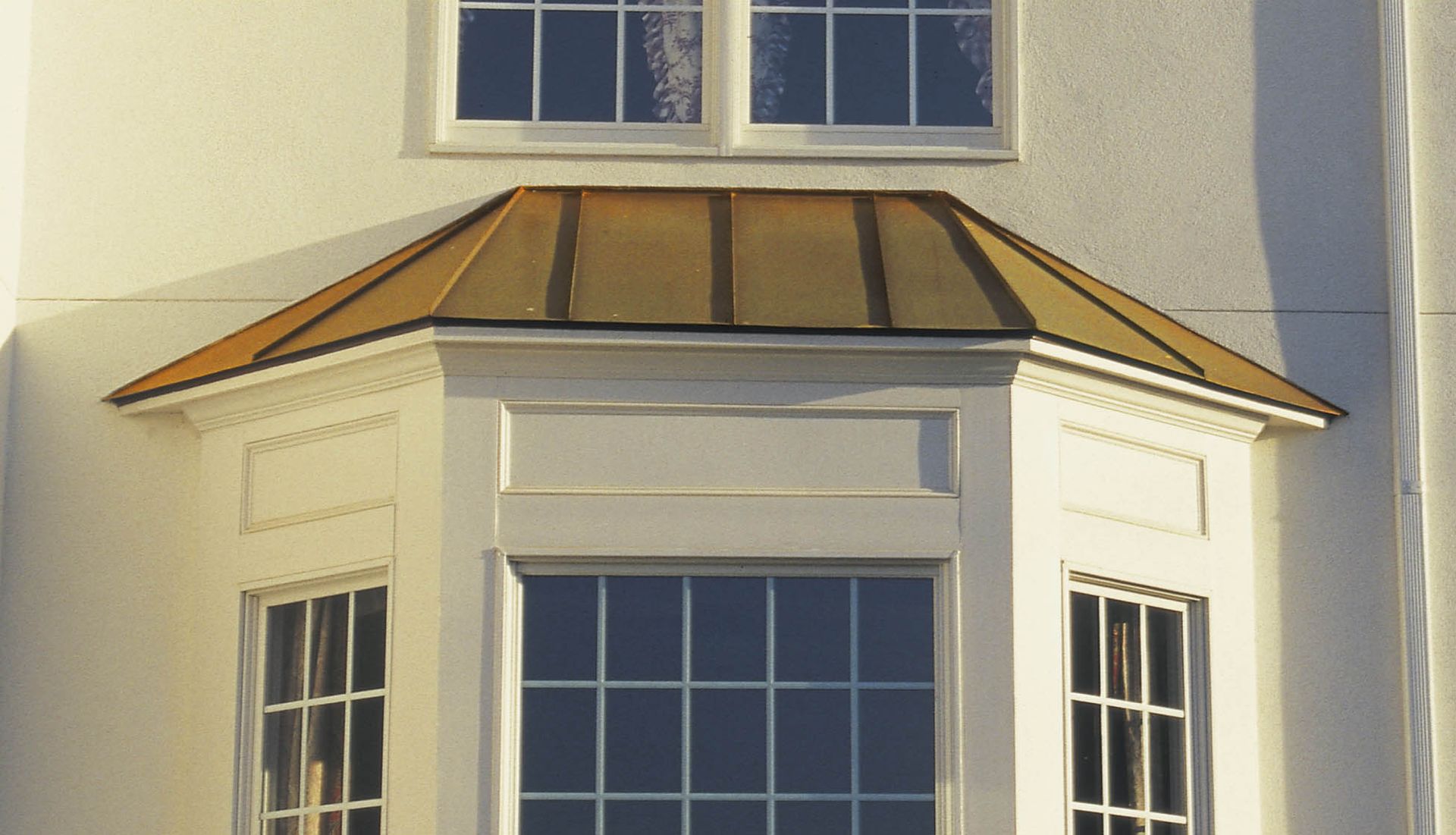 White bay window with copper roof on a cream house facade