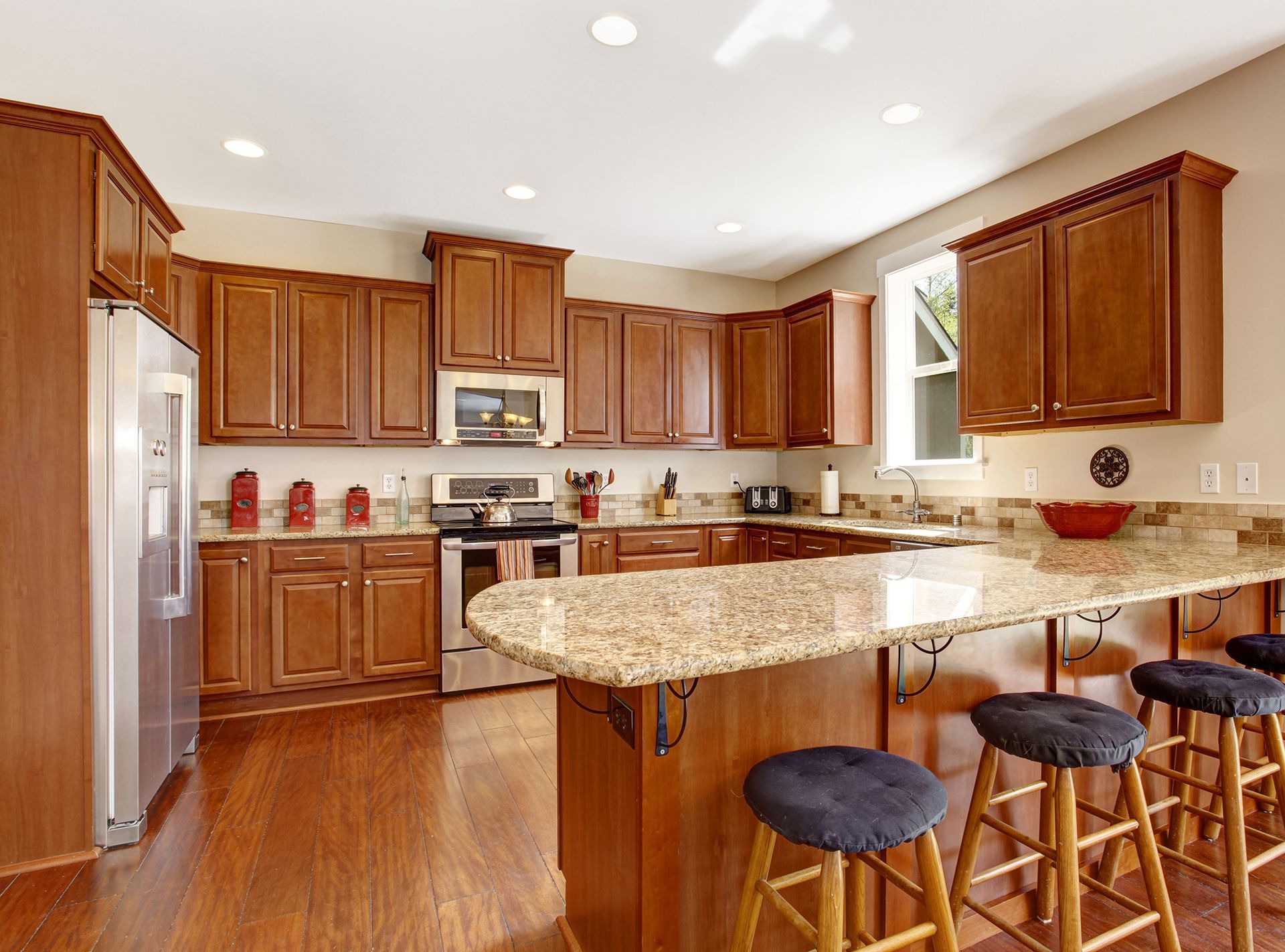 Bright kitchen with wood cabinets, granite island, stainless appliances, and three stools on hardwood floors