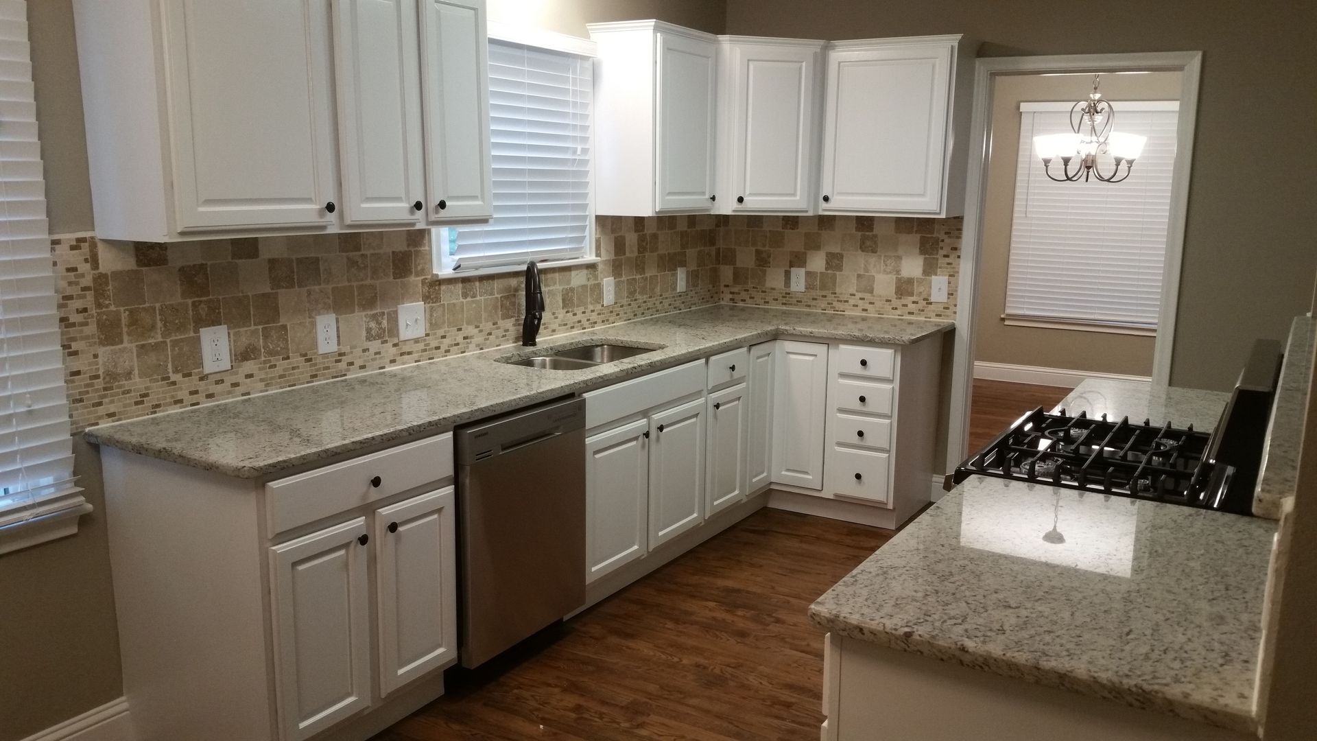 Bright kitchen with white cabinets, granite counters, stainless dishwasher, and hardwood floors.