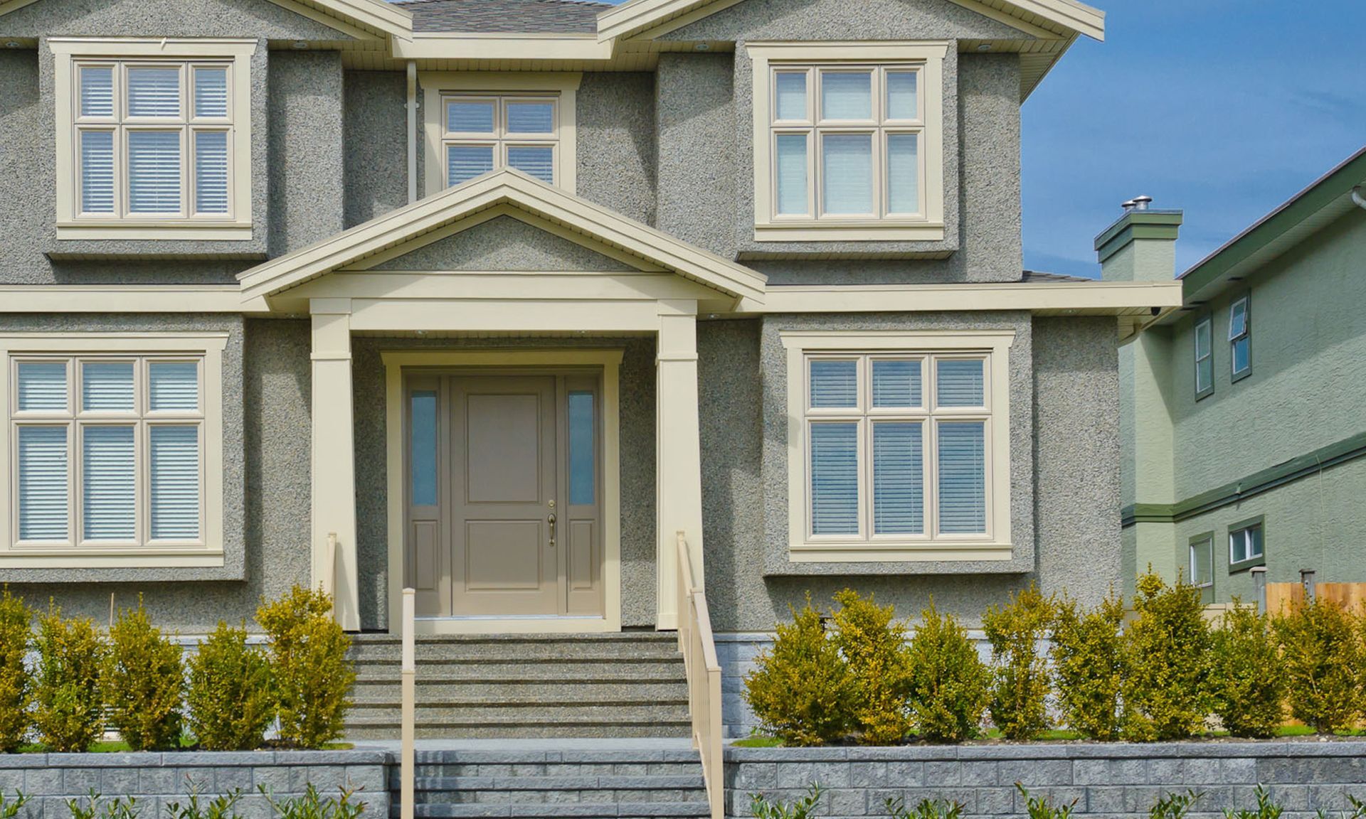 Two-story gray house with white trim, front steps, and a small garden in front