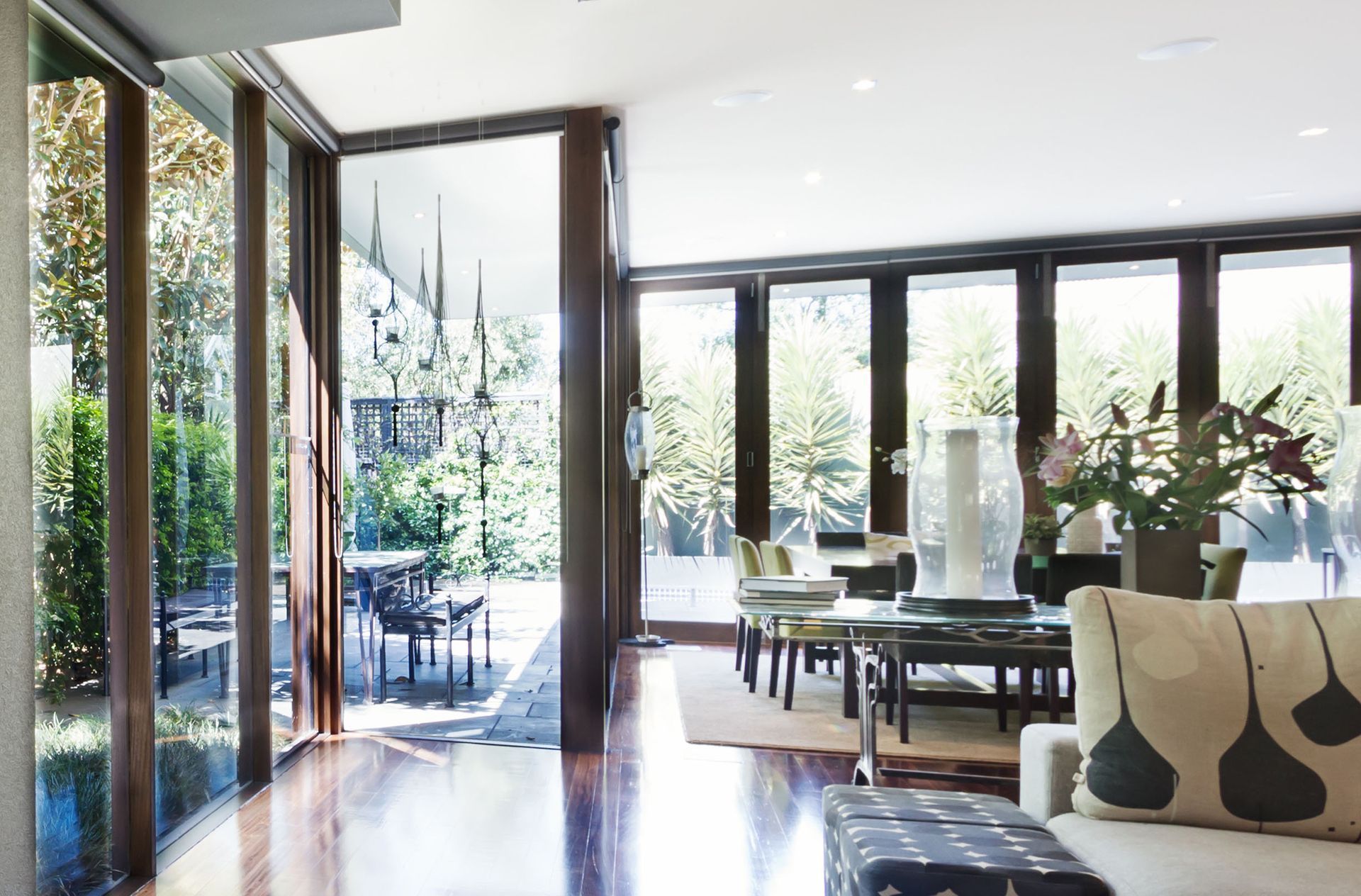 Bright modern living room with open glass doors, dark wood floor, and dining area overlooking a garden