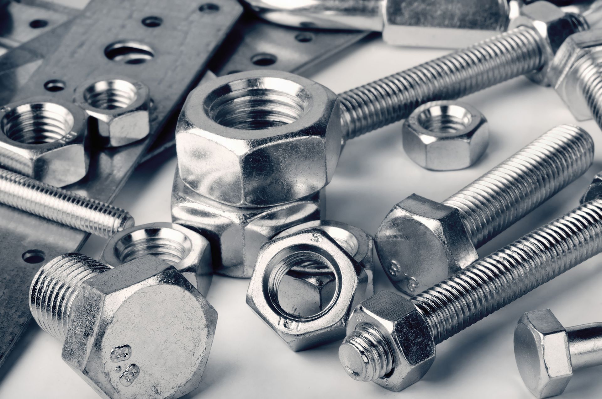 Assorted shiny metal bolts, nuts, and screws arranged on a white surface
