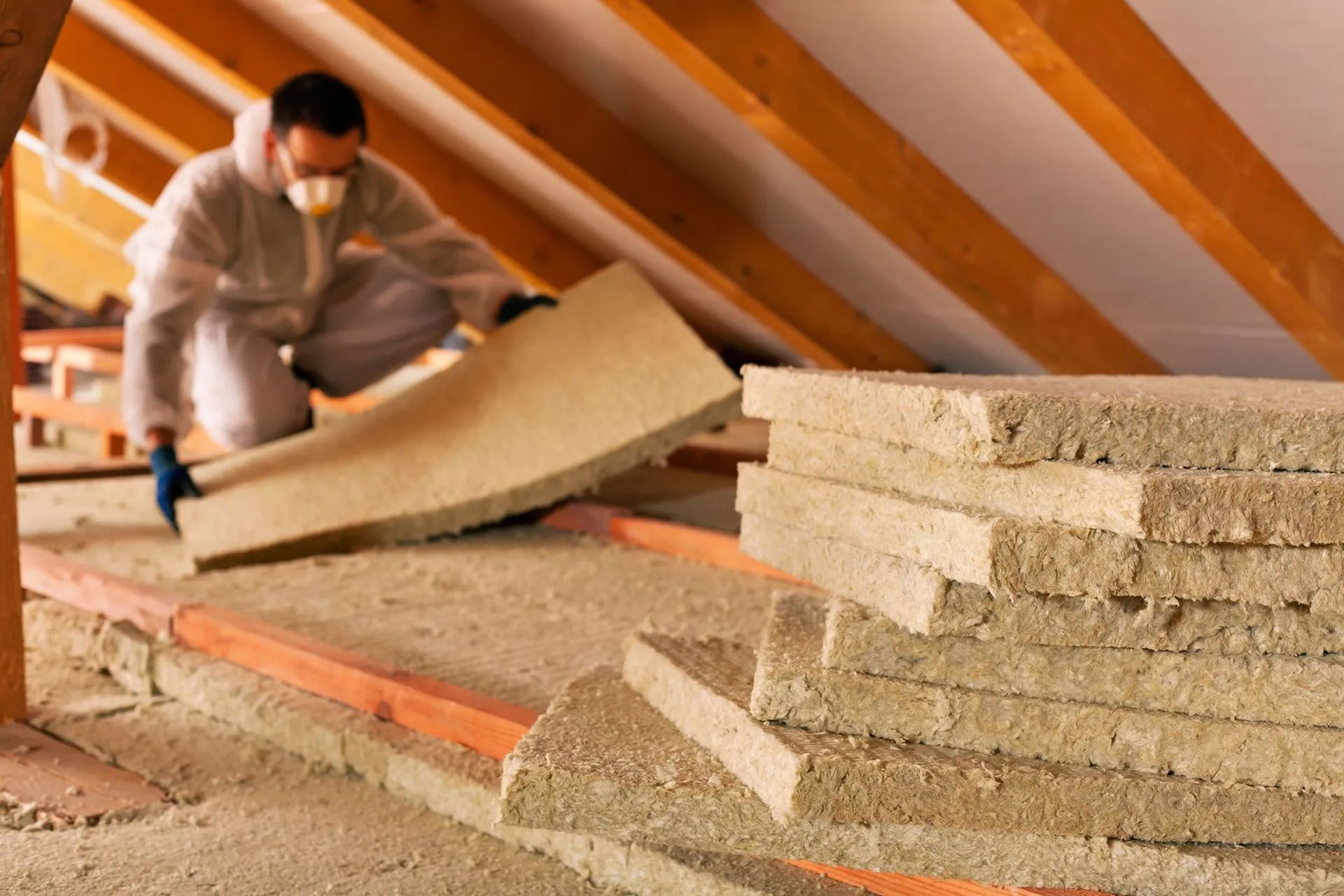 Worker in an attic installing insulation boards beside stacked material.