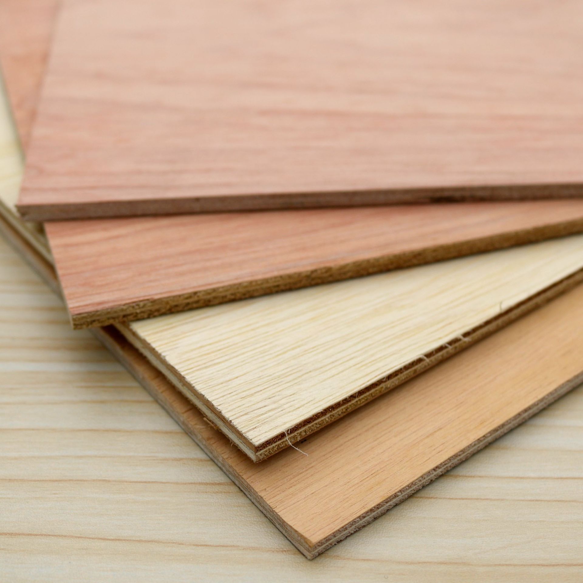 Stacked wood veneer sheets in pink, cream, and tan on a light wooden surface