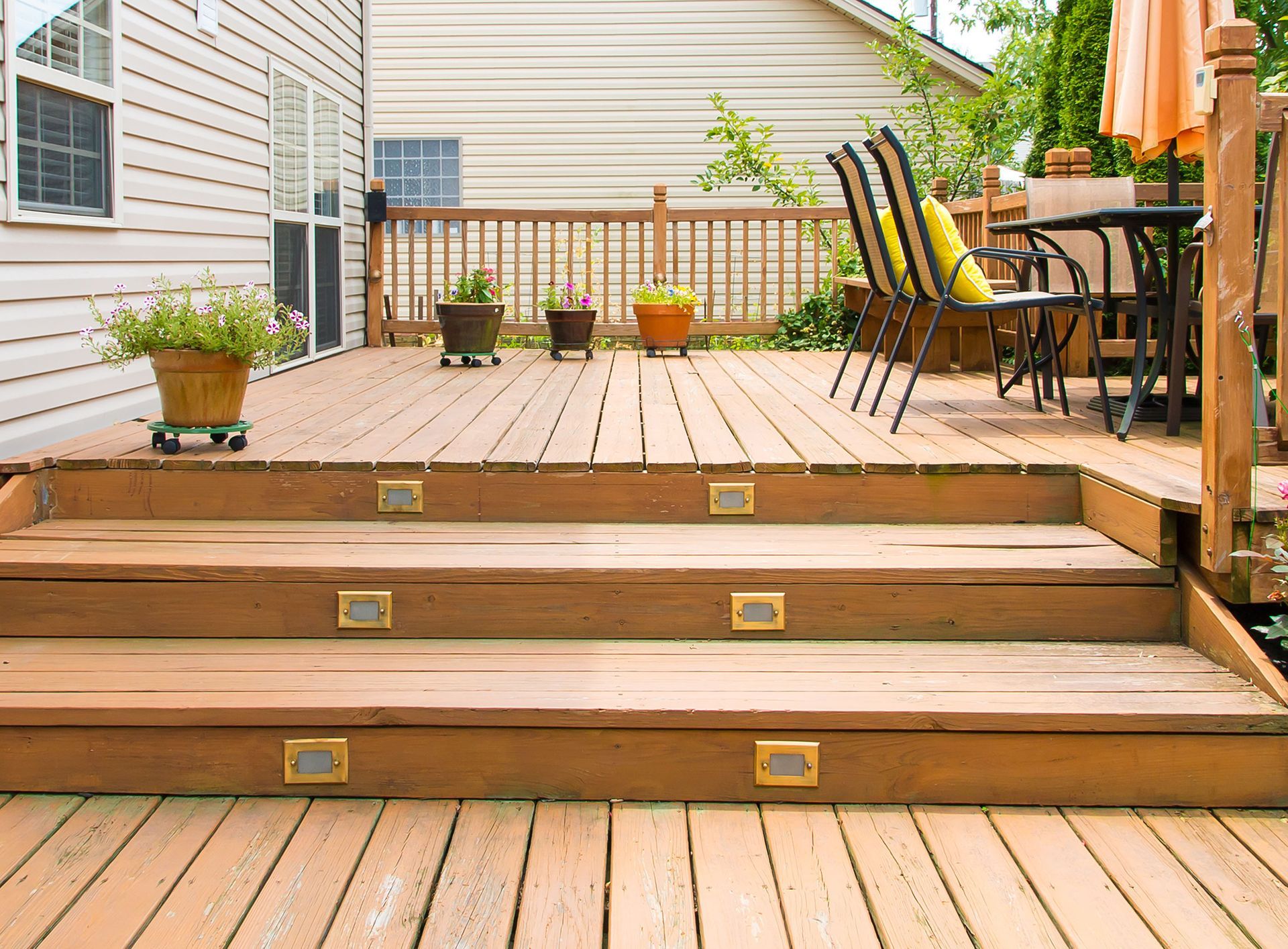 Wooden backyard deck with steps, potted plants, and patio furniture beside a house