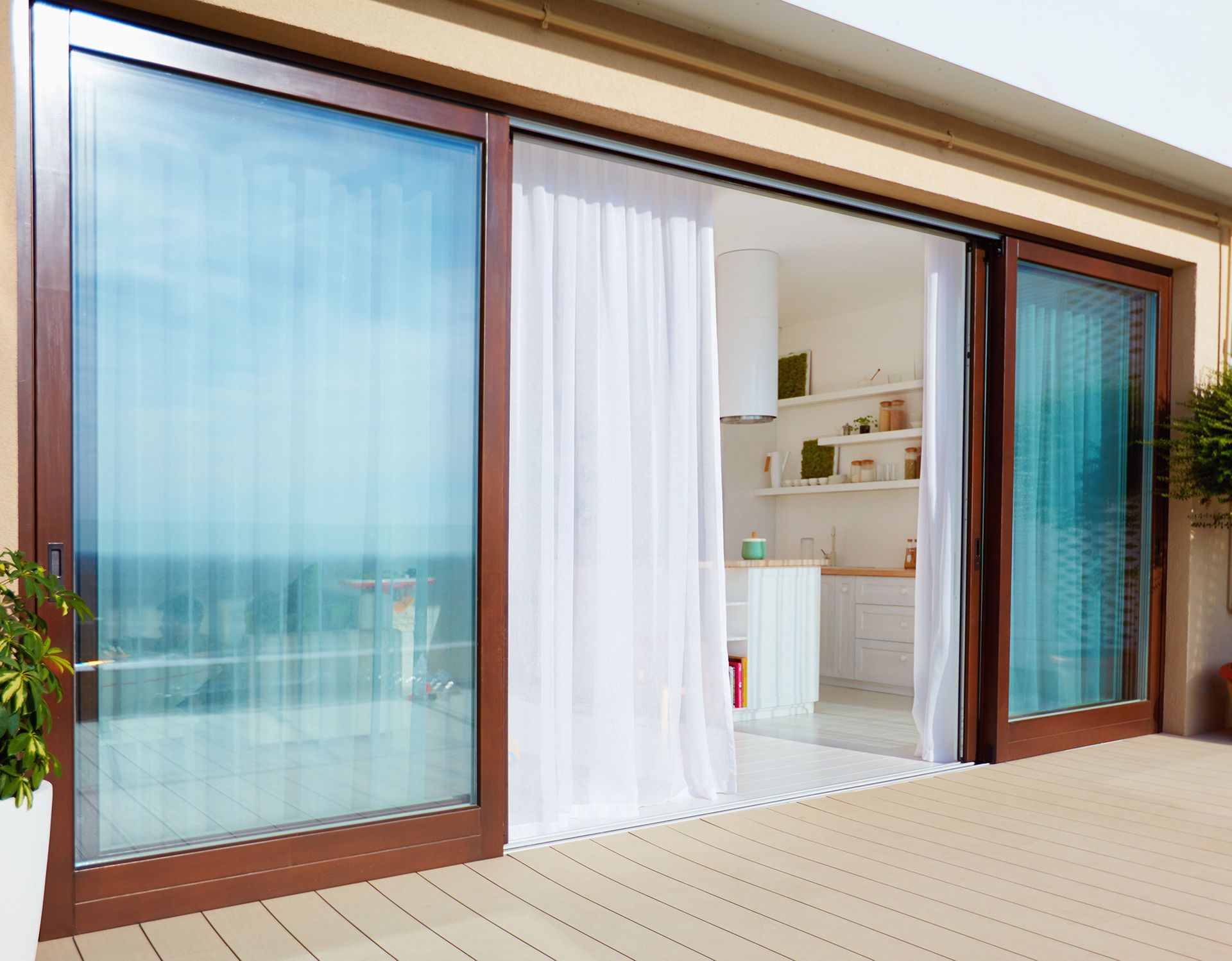 Sliding glass doors open to a bright balcony with white curtains and an ocean view.