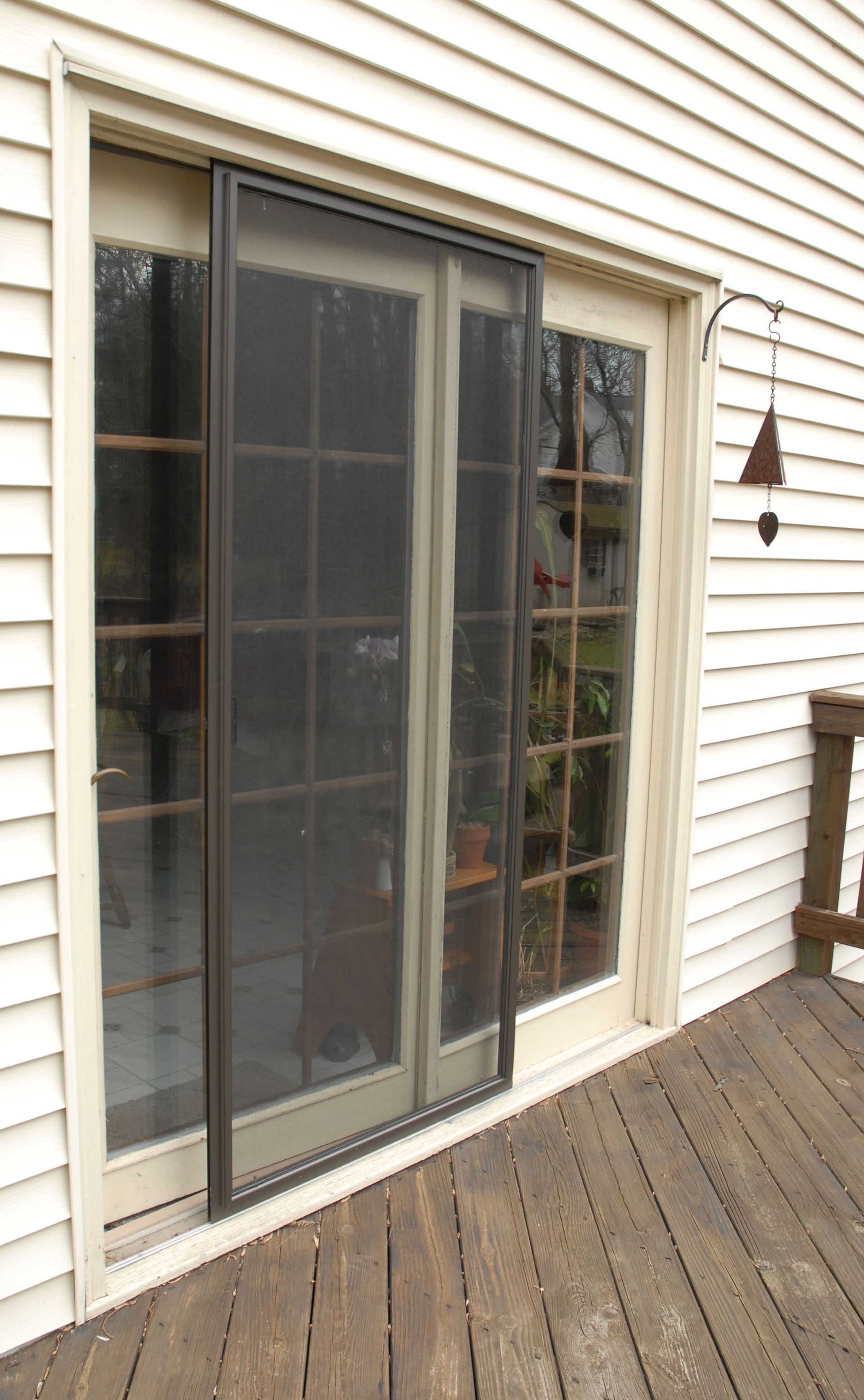 Sliding glass door with screen on a white-sided house, opening onto a wooden deck